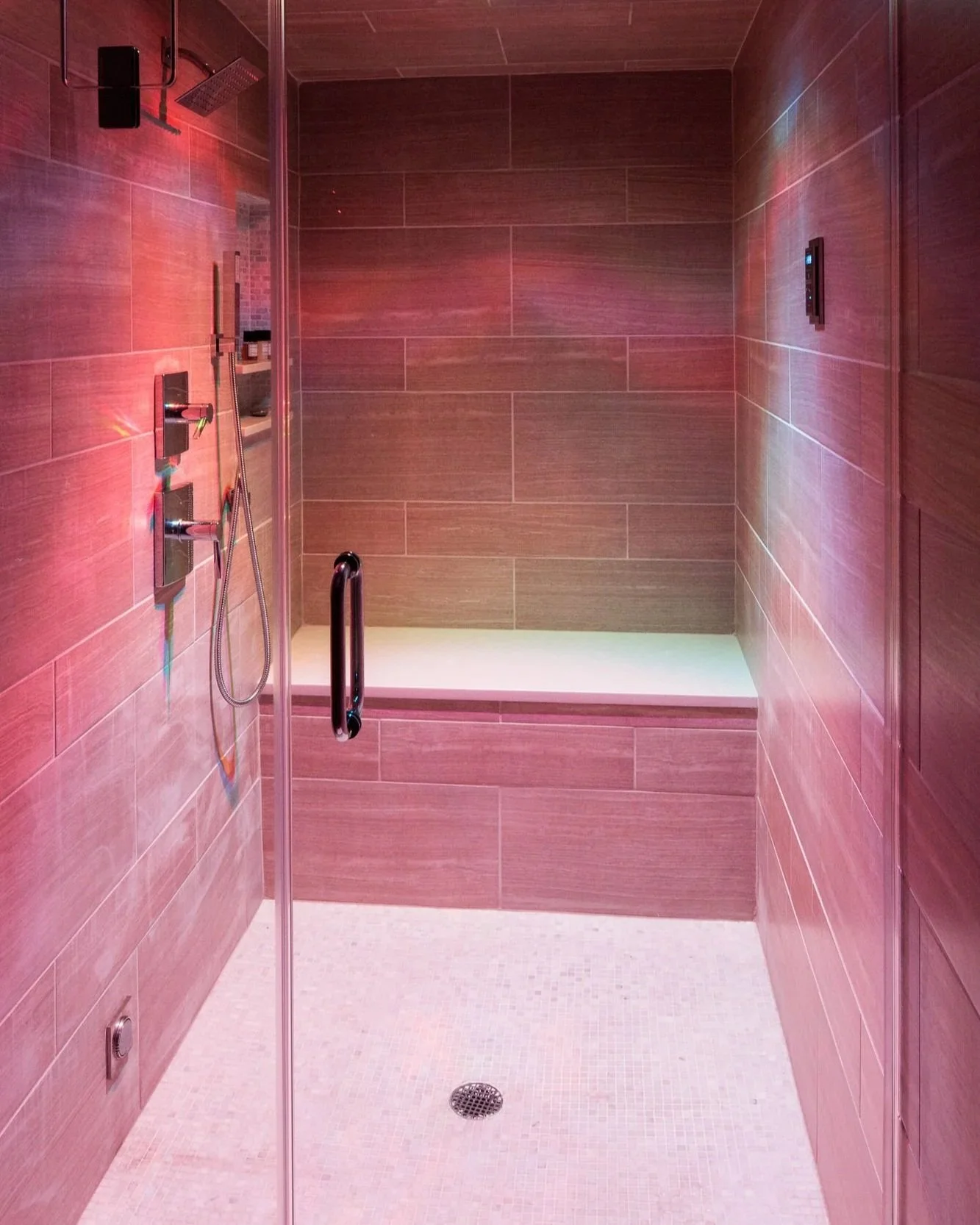Modern shower with LED lights, glass door, and tiled interior.