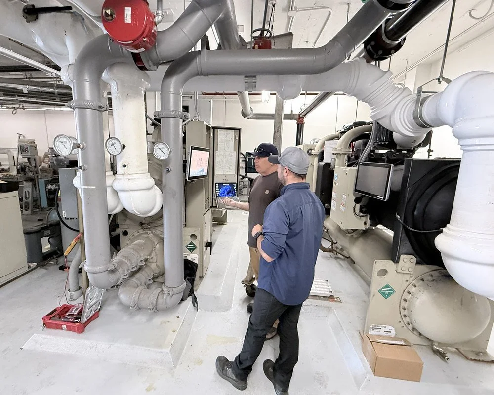 Two CCMS technicians reviewing trend data on a laptop beside a water-cooled chiller in a central plant