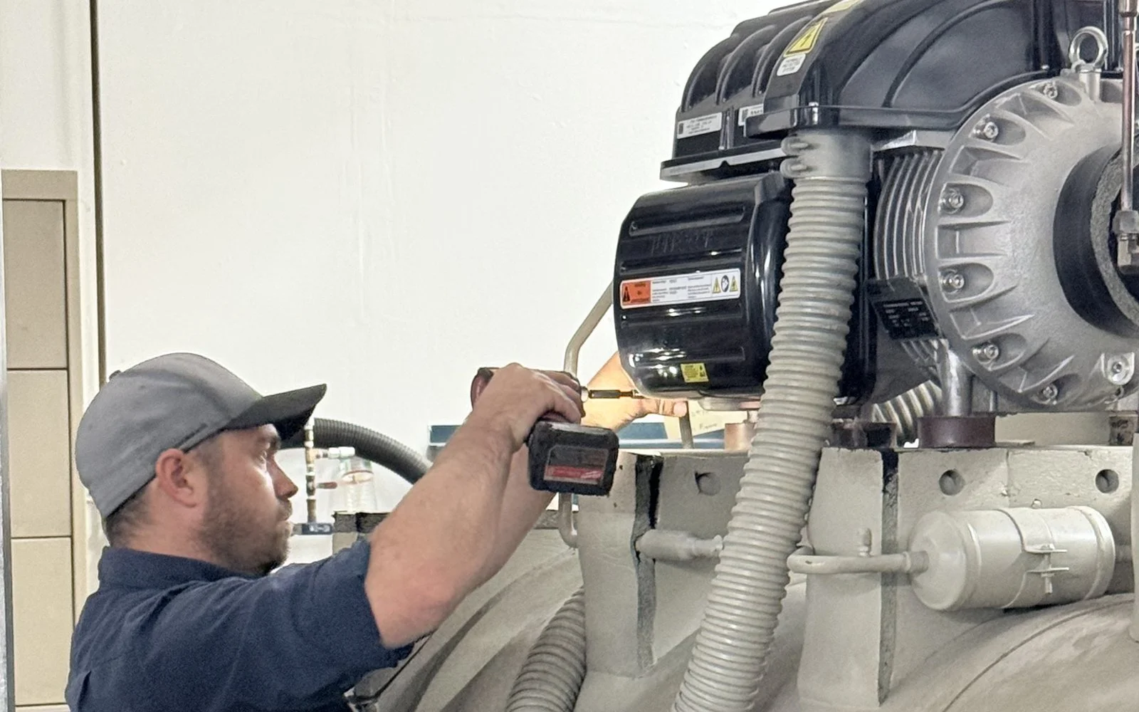 A CCMS technician working on a chiller compressor with a refrigerant recovery unit running beside him