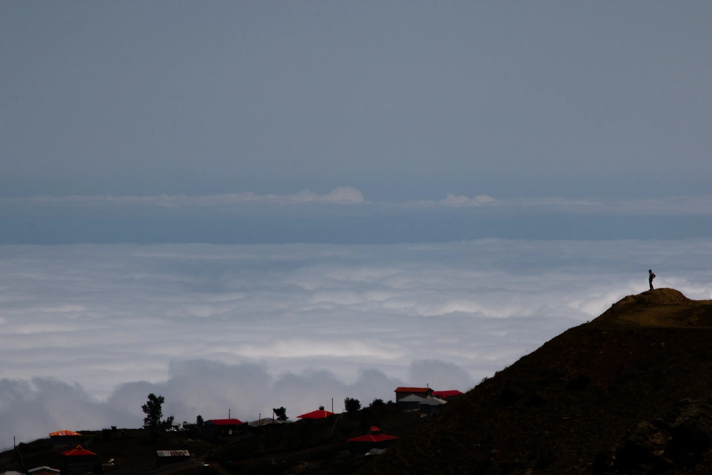 A lone figure stands on top of a mountain overlooking a sea of clouds. Photo taken in a village in Iran by Freshte Javid.