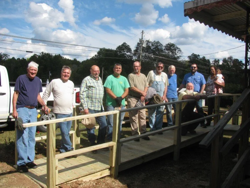 Group of people standing on a newly built wooden ramp outdoors, smiling for the photo on a sunny day.