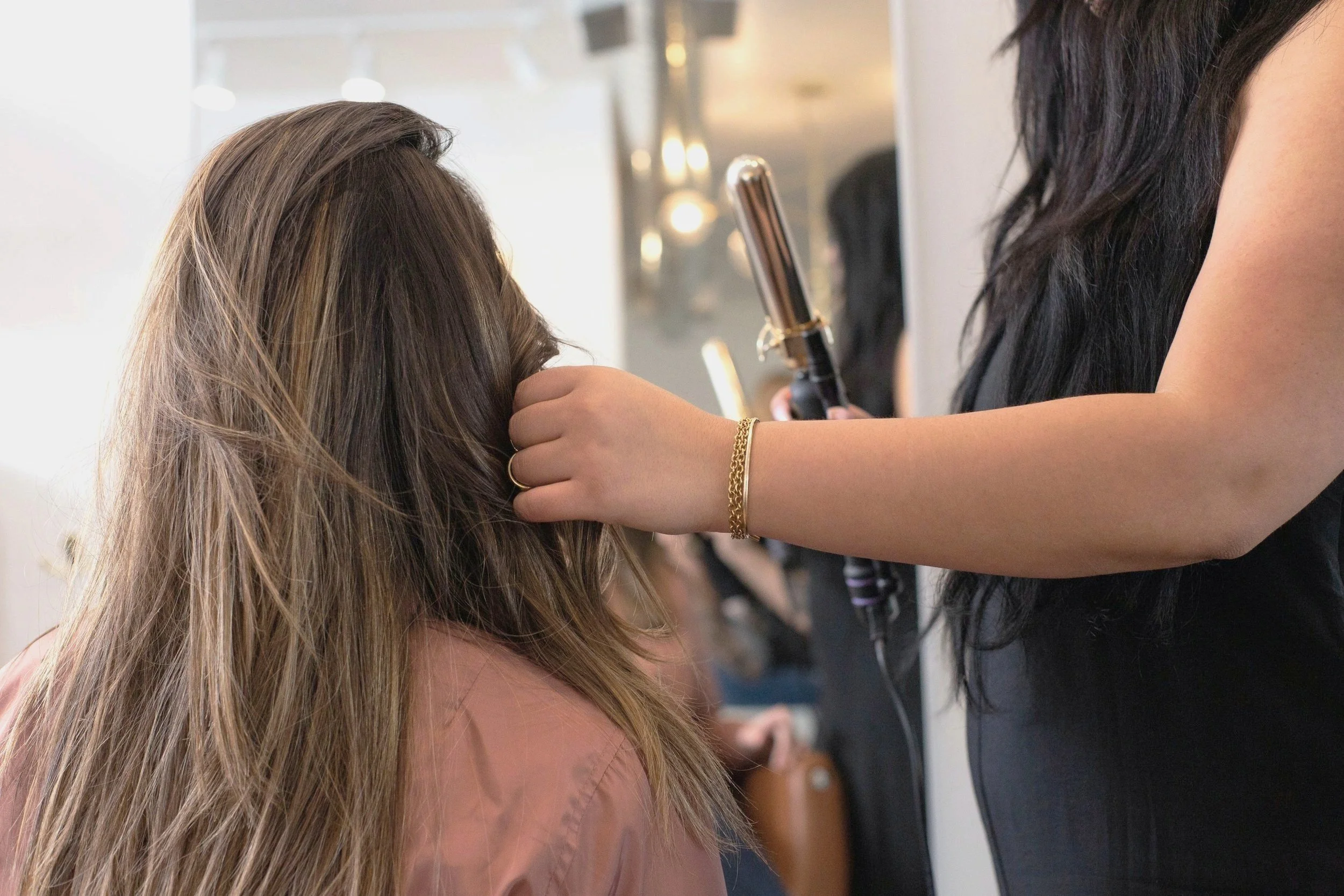 A hairstylist curling a woman's hair with a curling iron in a salon.