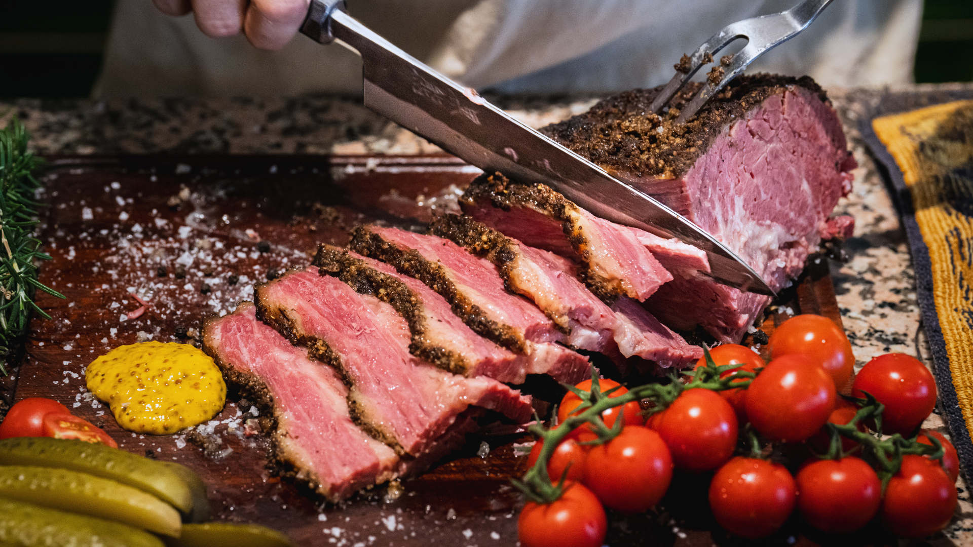 Pastrami being sliced on a wooden board into thick-cut tender-looking pieces. Image showcases the pinky inside and crusty bark on the outside.