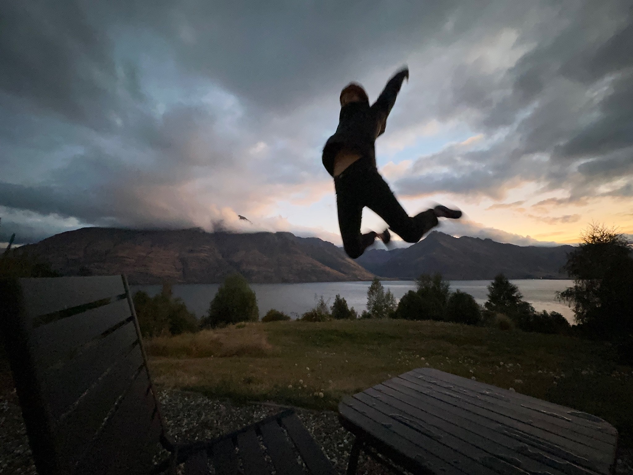 Blurry image of a girl jumping with Lake Wakatipu in Queenstown, New Zealand in the background.