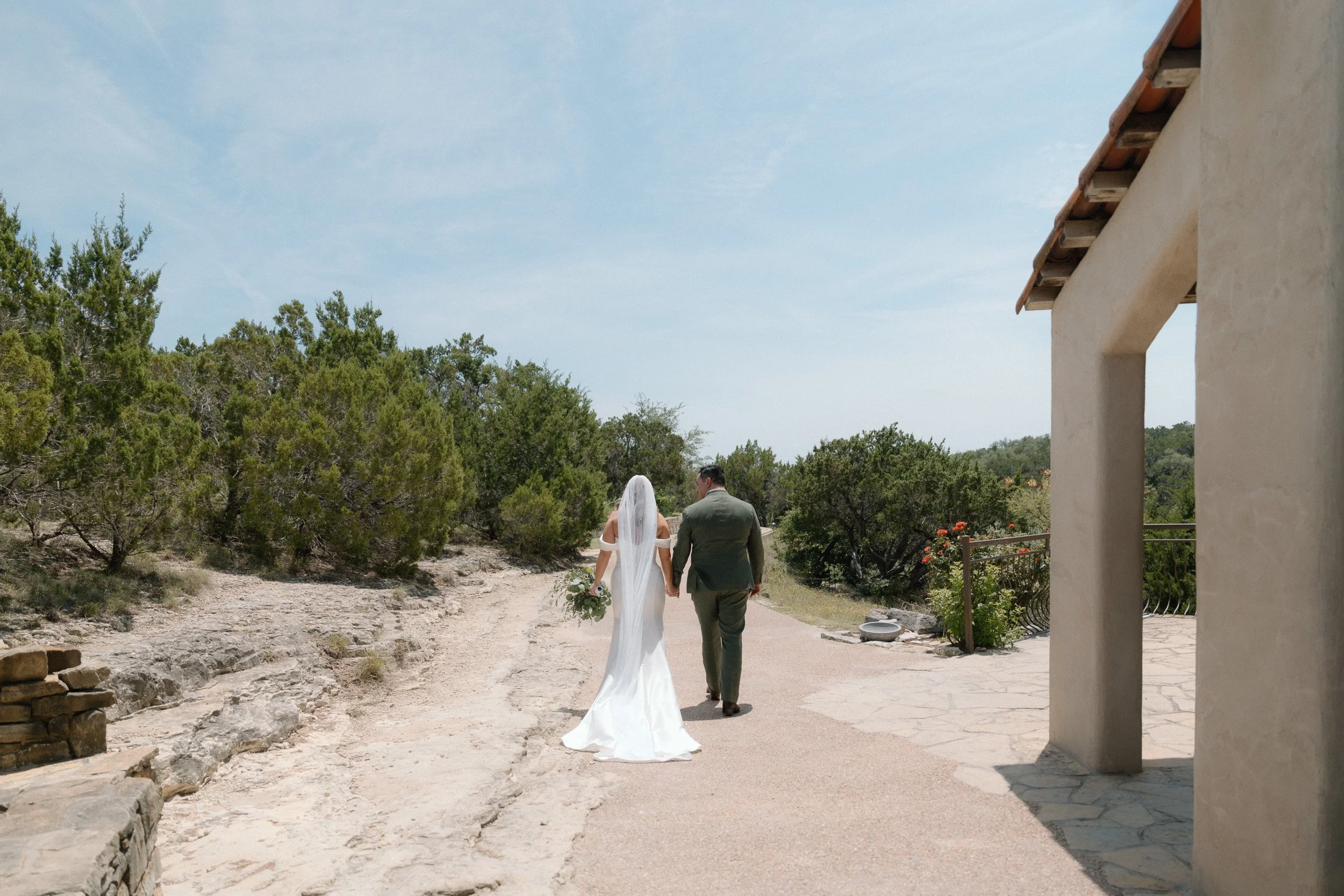 Bride and groom walk hand in hand down a path with sweeping Texas Hill Country views after the ceremony