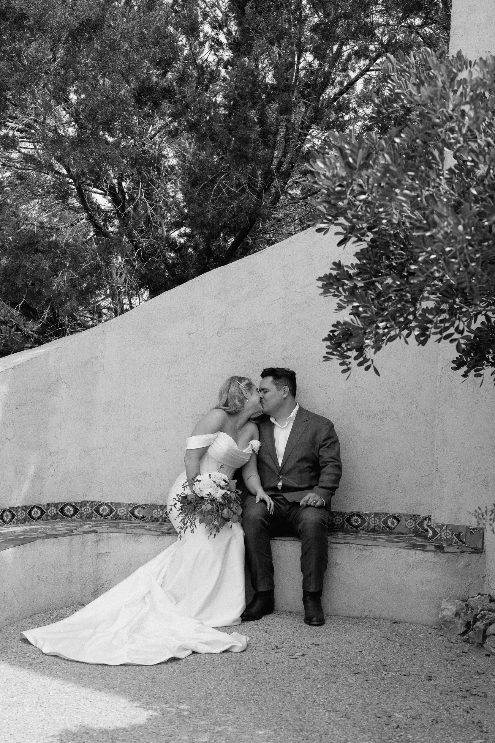 The couple kisses on a curved tiled bench with the bride's train spread across the ground, in black and white