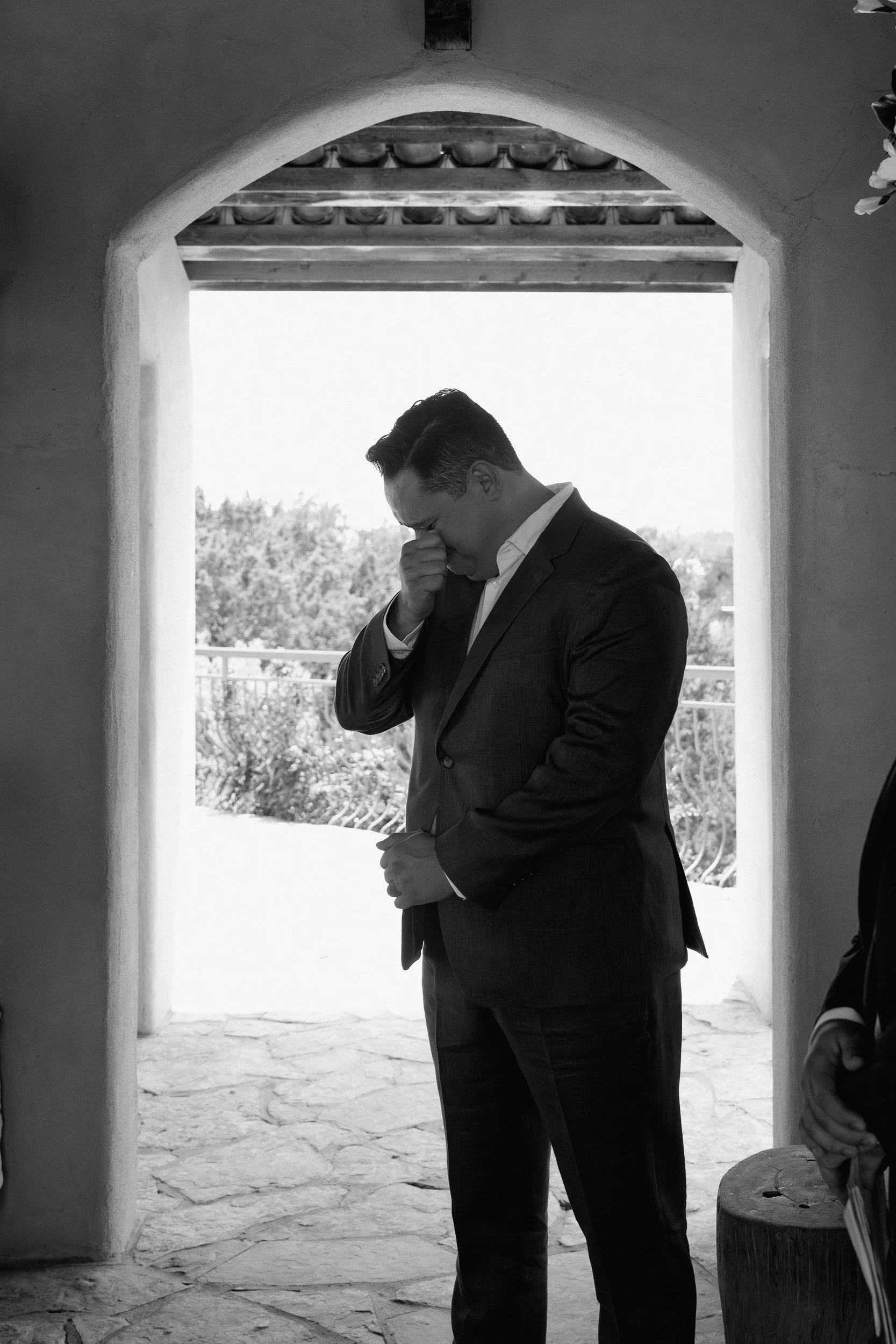Groom wipes away tears under a stone archway as his bride walks down the aisle at Chapel Dulcinea