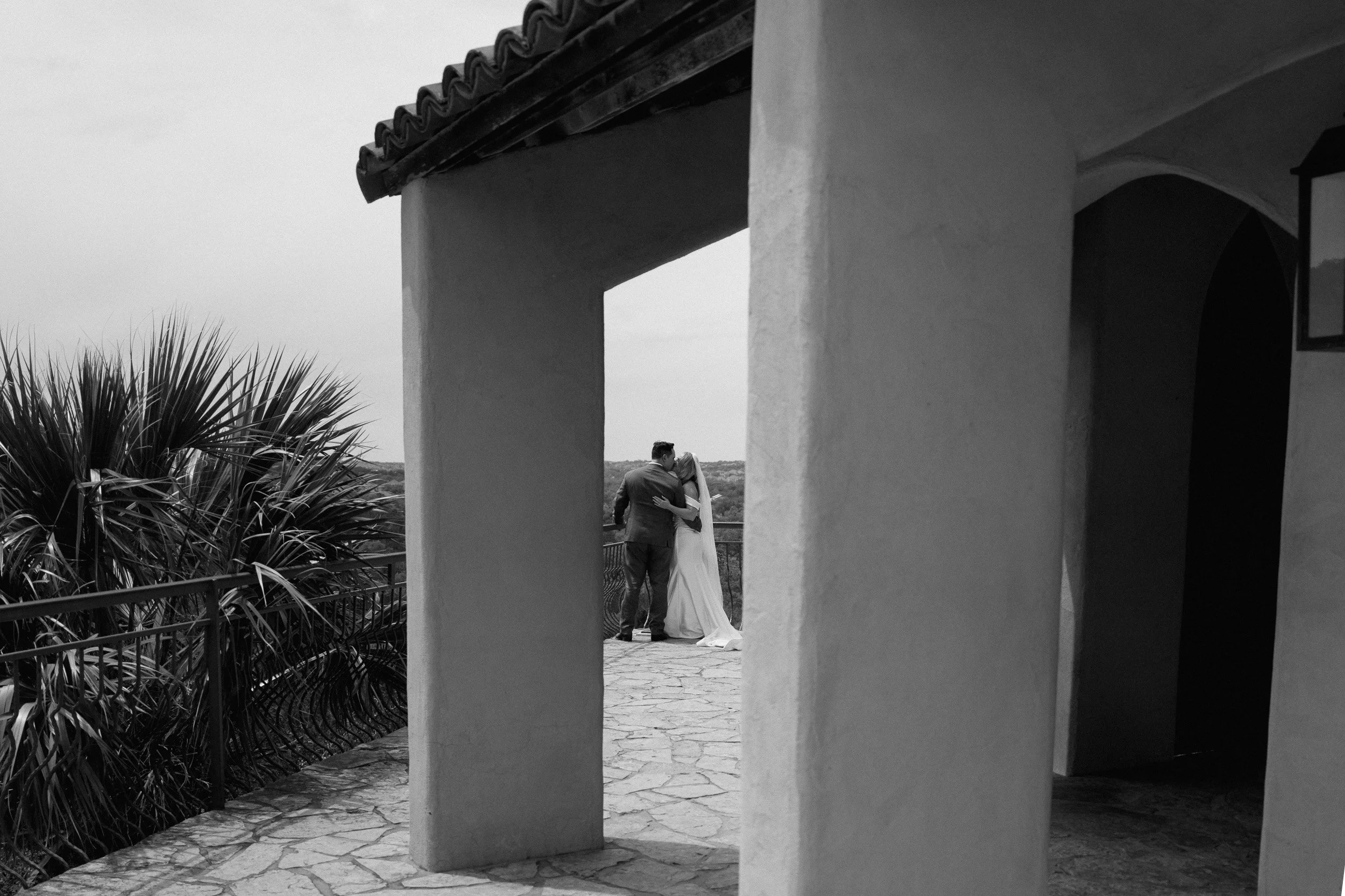 Black and white photo of the couple kissing at the overlook, framed by the chapel's columns