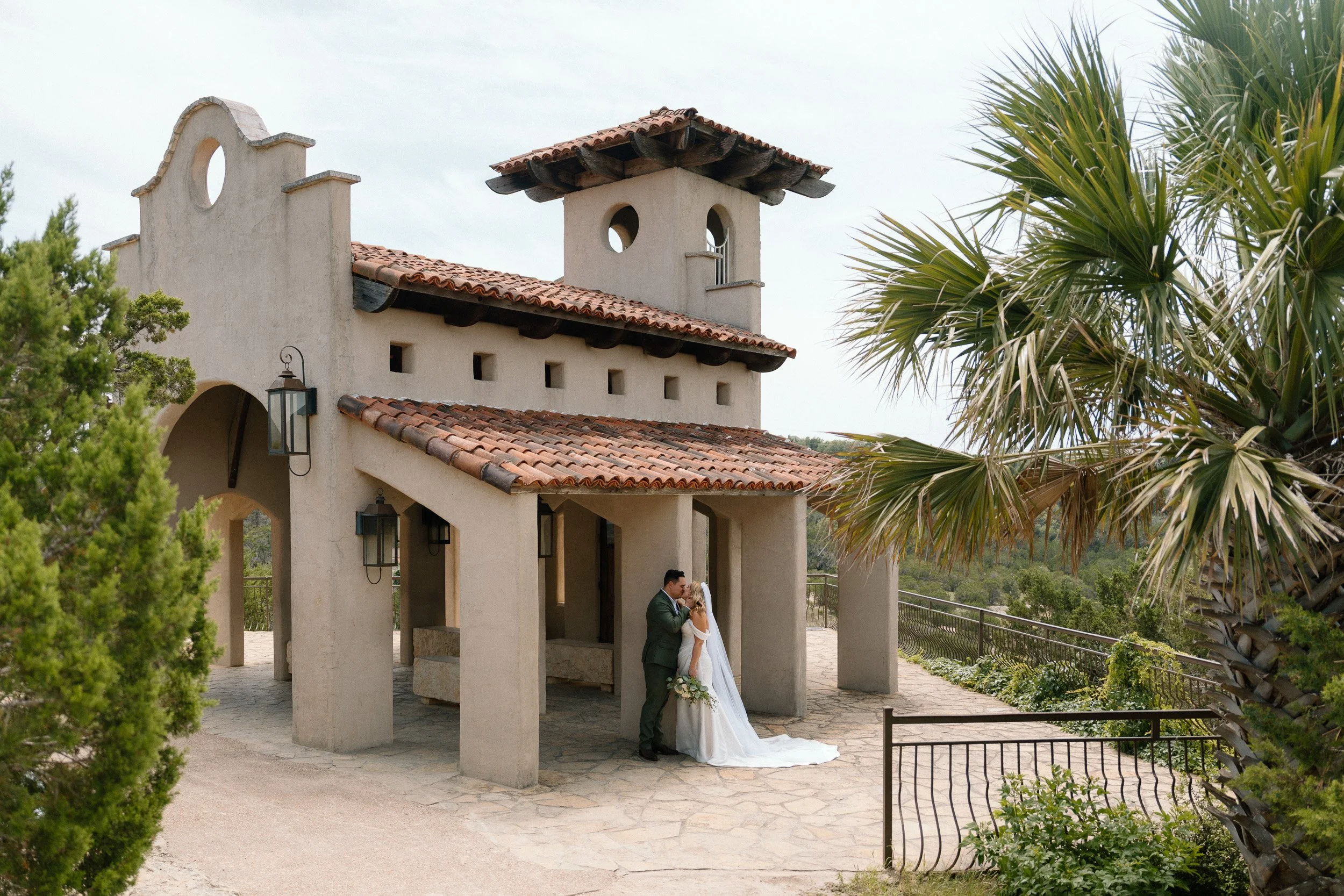 Wide view of the Spanish-style Chapel Dulcinea exterior as the couple kisses beneath the colonnade