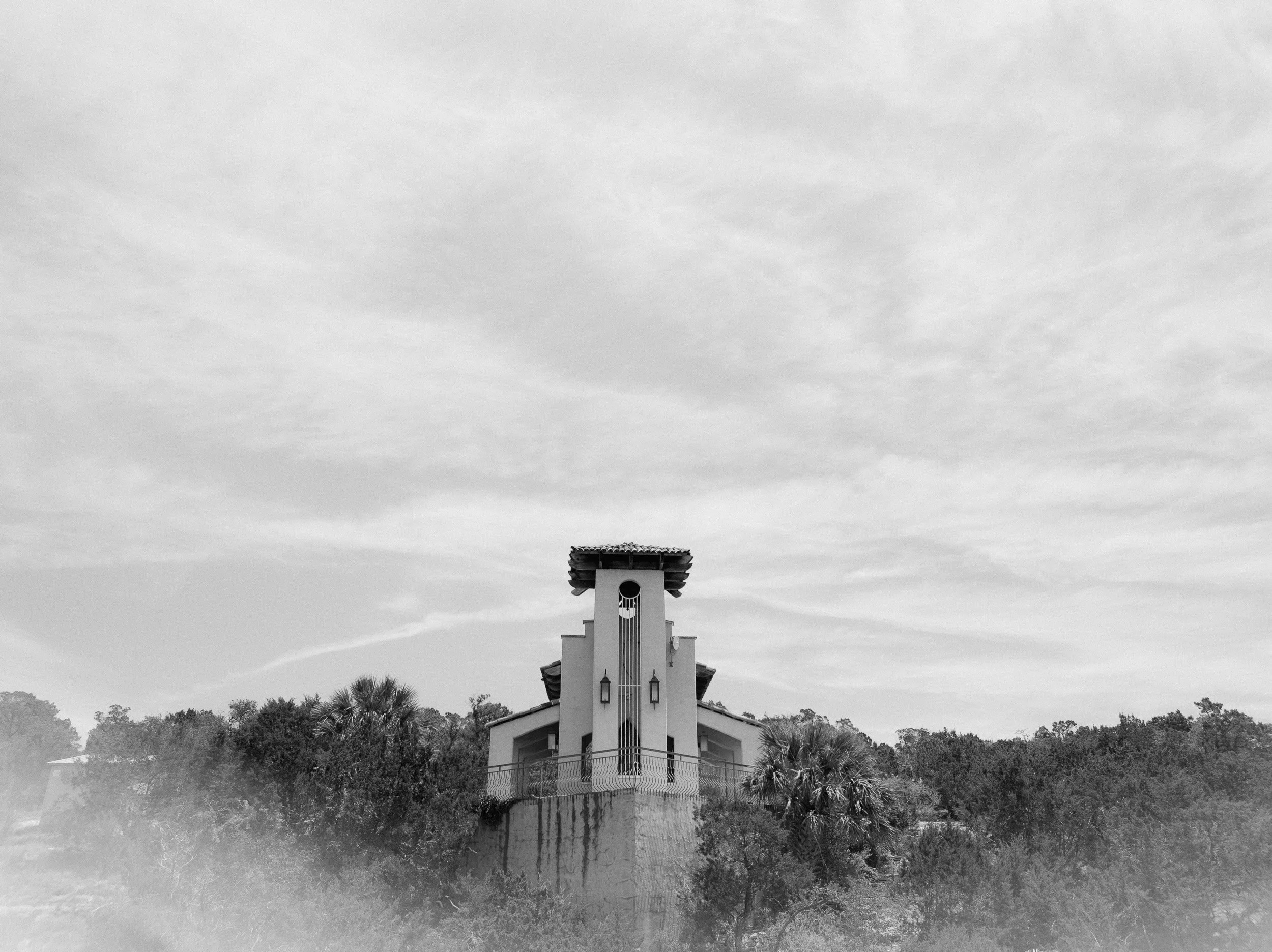 Black and white view of the Chapel Dulcinea bell tower rising above the Texas Hill Country tree line