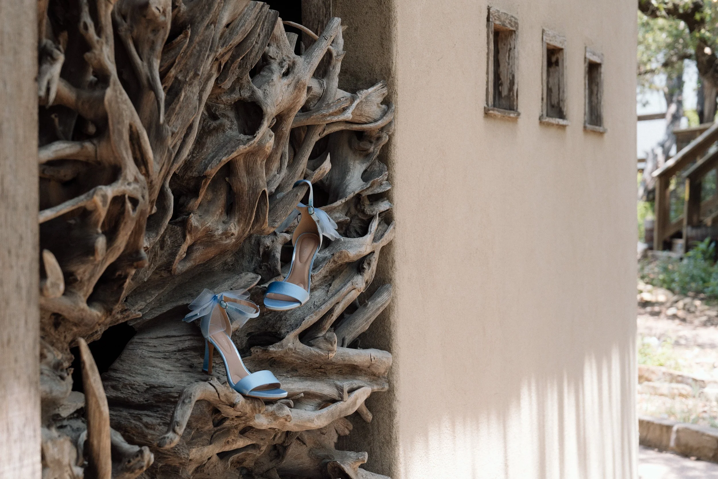 Pale blue bridal heels with tulle ankle bows resting on a sculptural driftwood wall