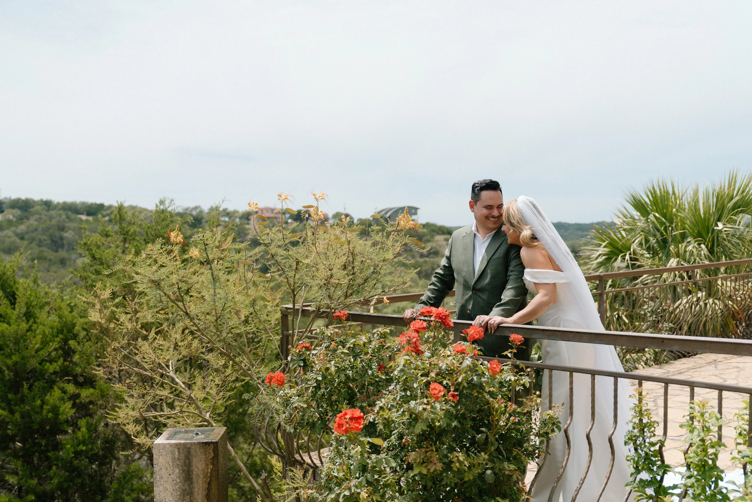 Smiling together, the couple pauses at a balcony railing overlooking the Texas Hill Country