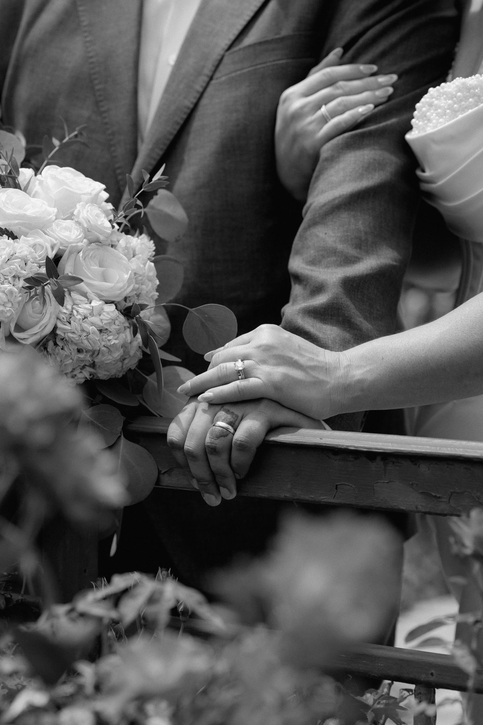 Black and white detail of the couple's hands and wedding rings resting on a railing
