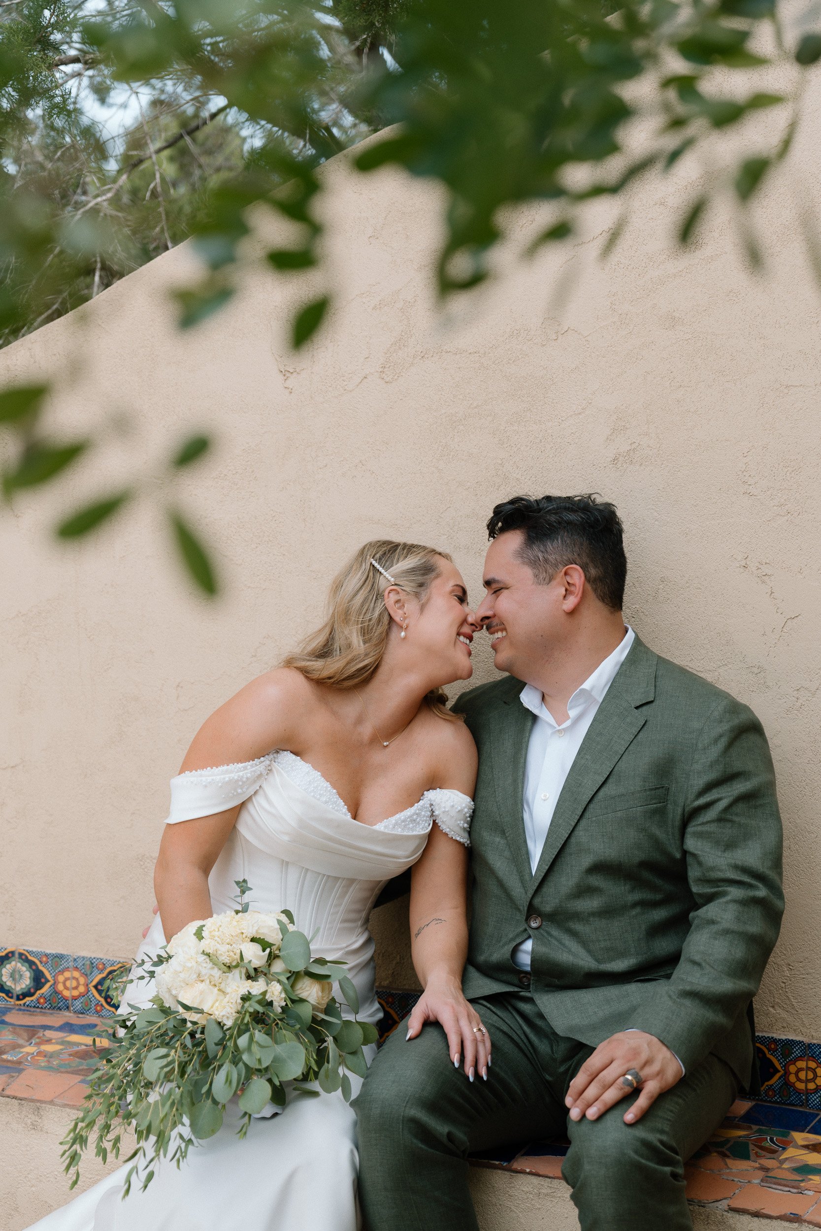 Bride and groom sit close and smile nose to nose on a colorful tiled bench at Chapel Dulcinea