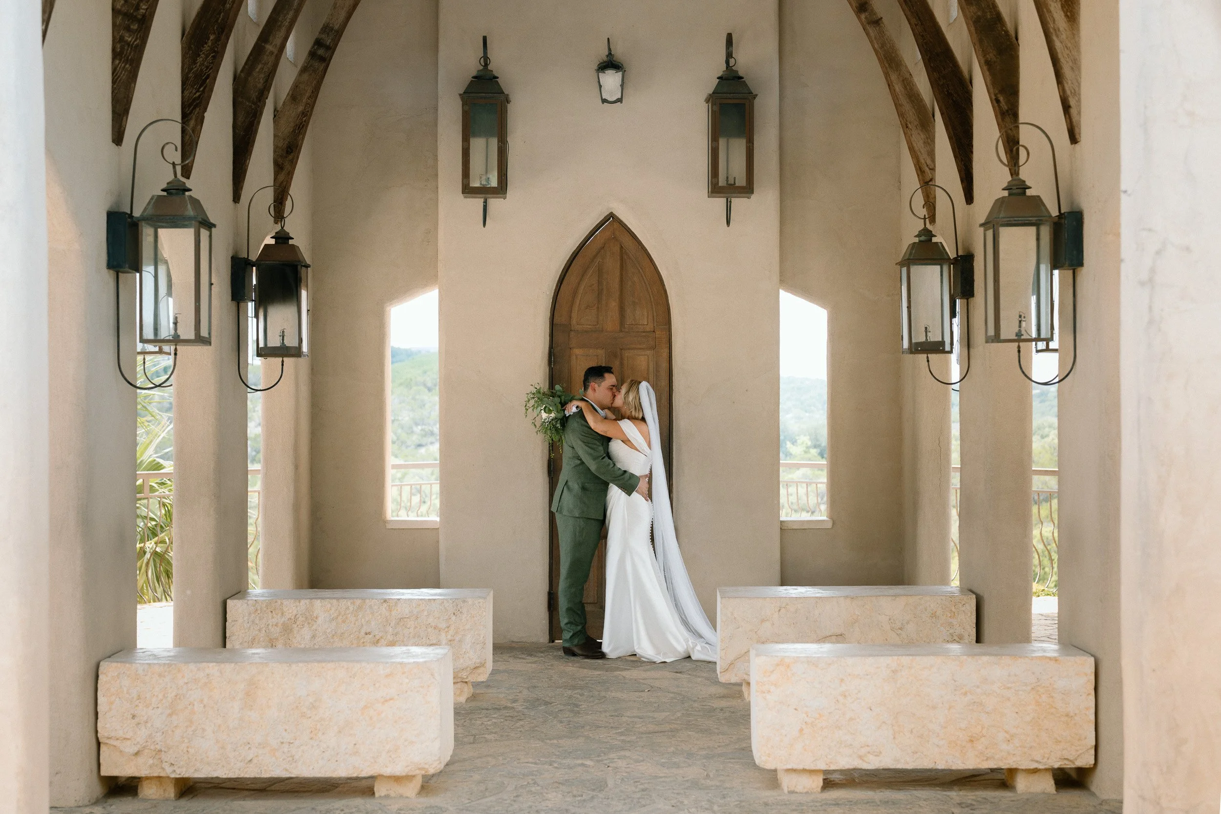 Wide view of the newlyweds kissing in the open-air chapel with stone benches and lanterns at Chapel Dulcinea