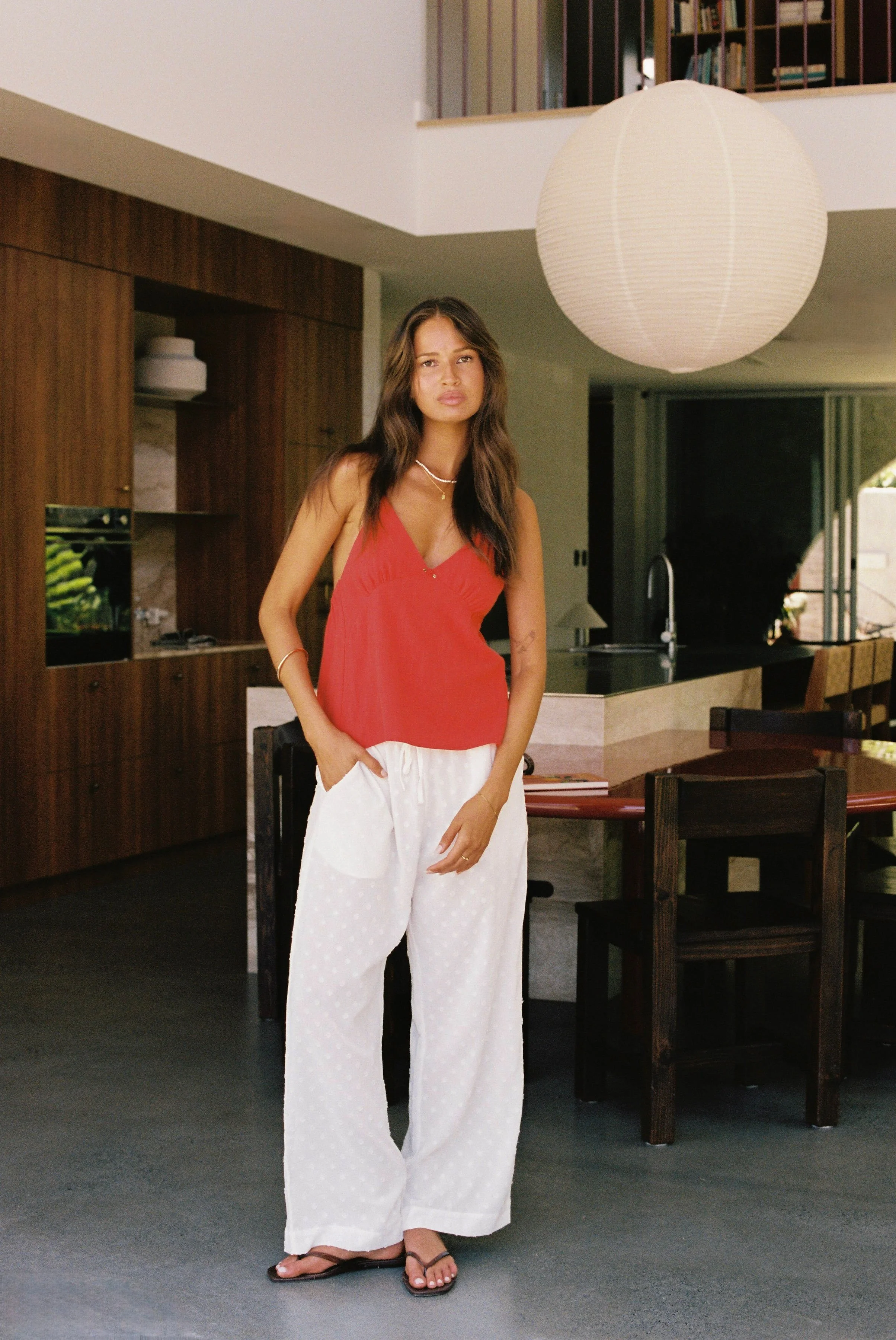 Women standing in a house with white pants and a red top from Rhythm. 