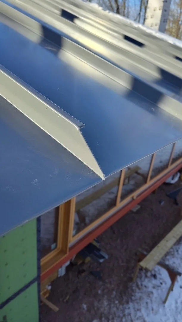 Close-up of a metal roof edge on a building under construction, with snow on the ground below.