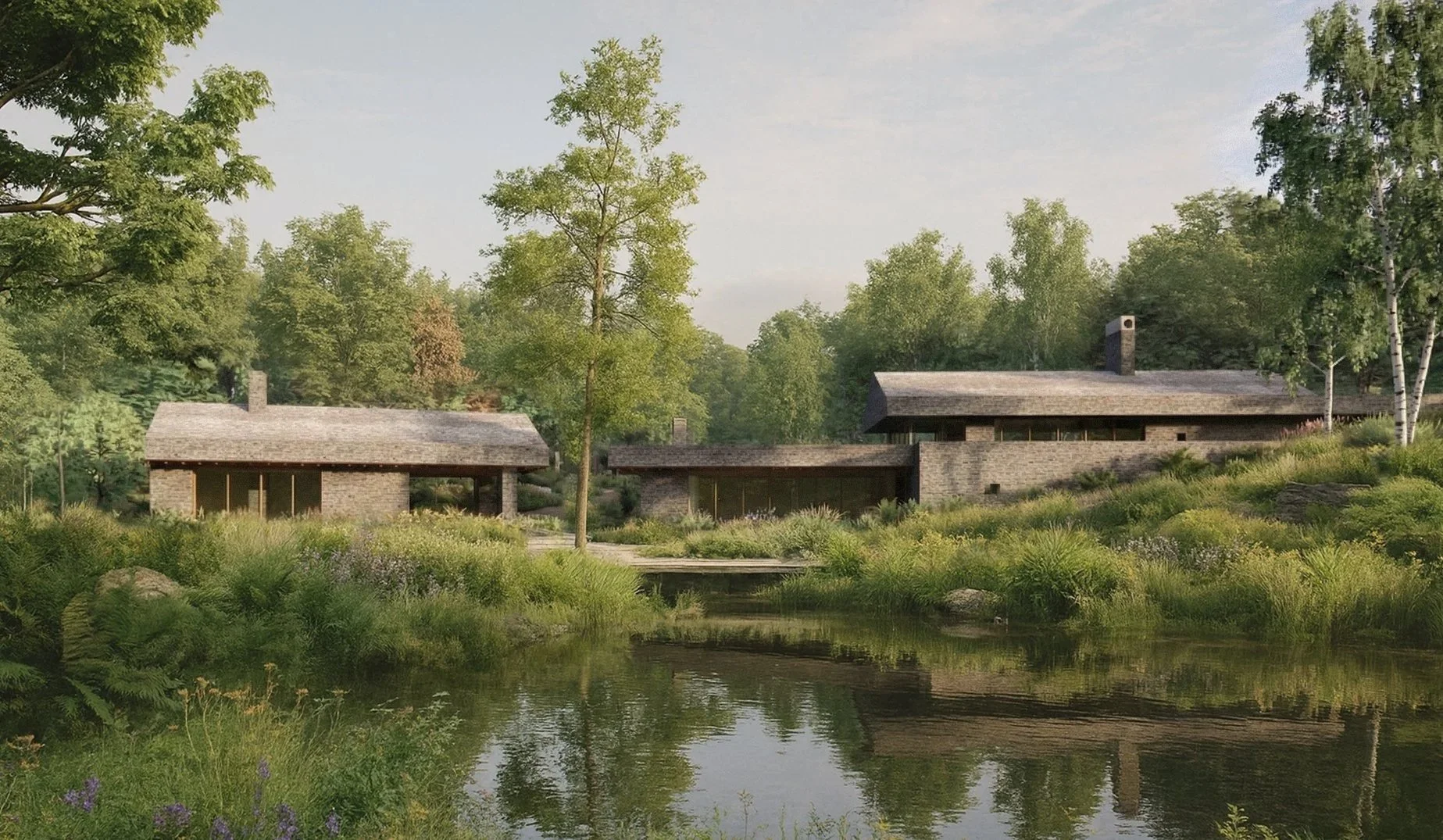 Two modern houses with stone exteriors are situated in a lush green landscape with a calm body of water reflecting the scene, surrounded by trees and vegetation.