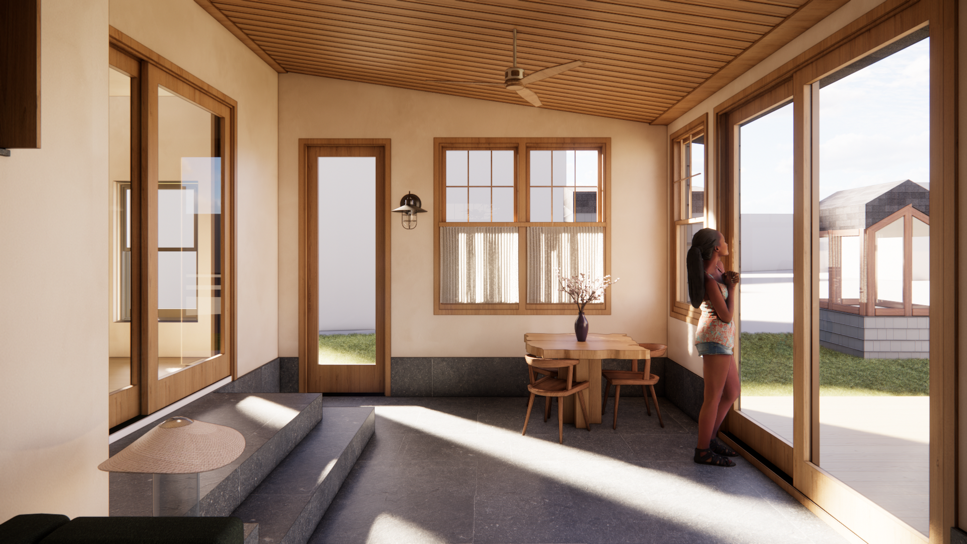 A woman standing inside a sunlit room with large windows, looking outside on a porch with grass and houses in the background.