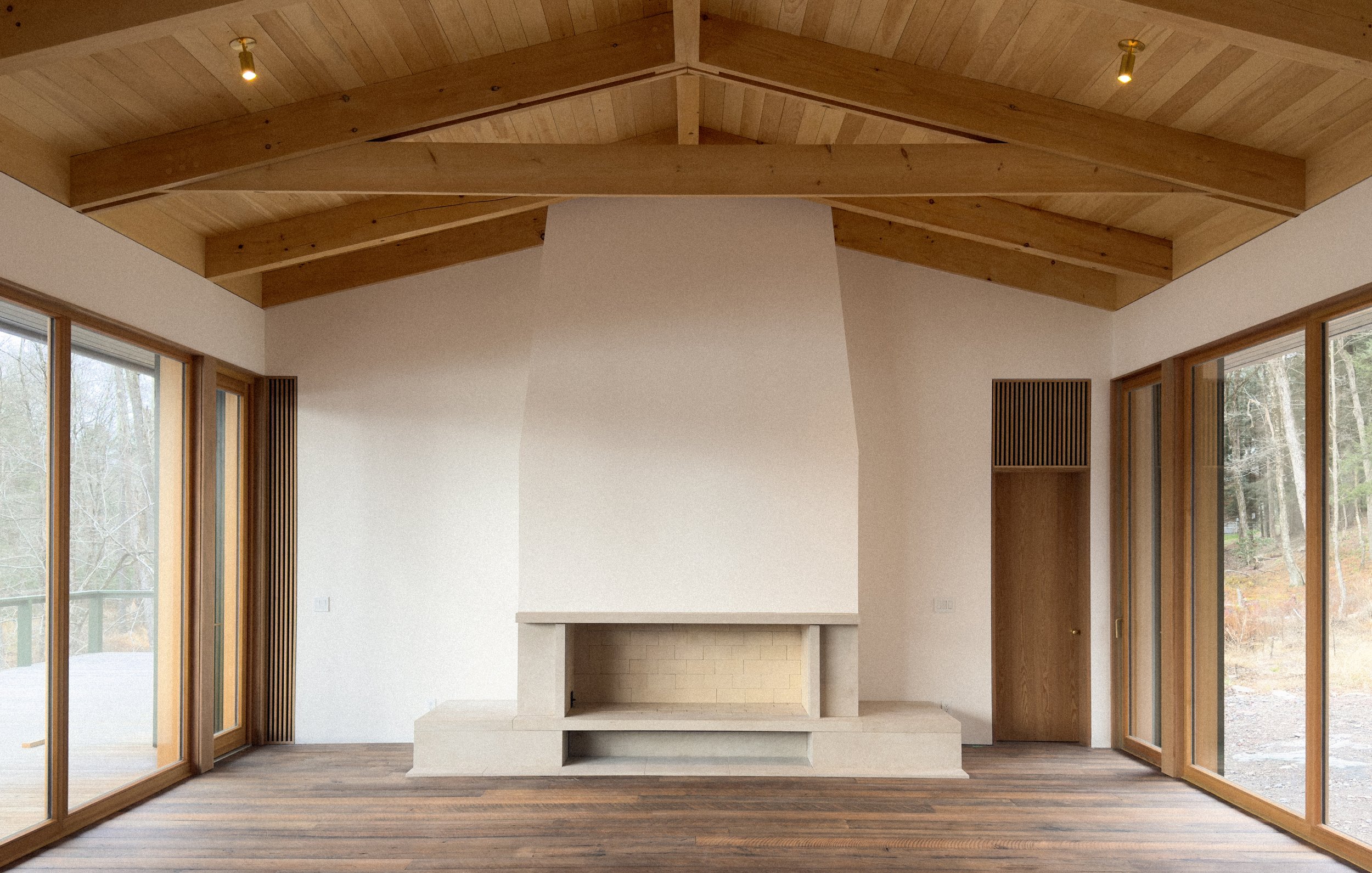 A modern living room with a central fireplace, large glass sliding doors on both sides, a wooden ceiling with exposed beams, and hardwood floors.