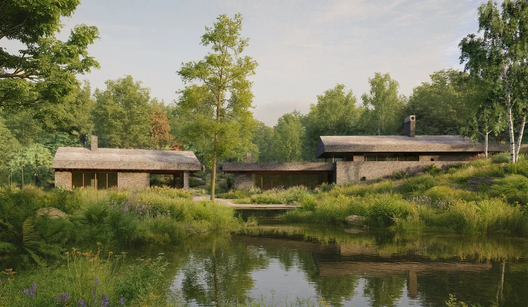 Two modern houses with stone exteriors are situated in a lush green landscape with a calm body of water reflecting the scene, surrounded by trees and vegetation.