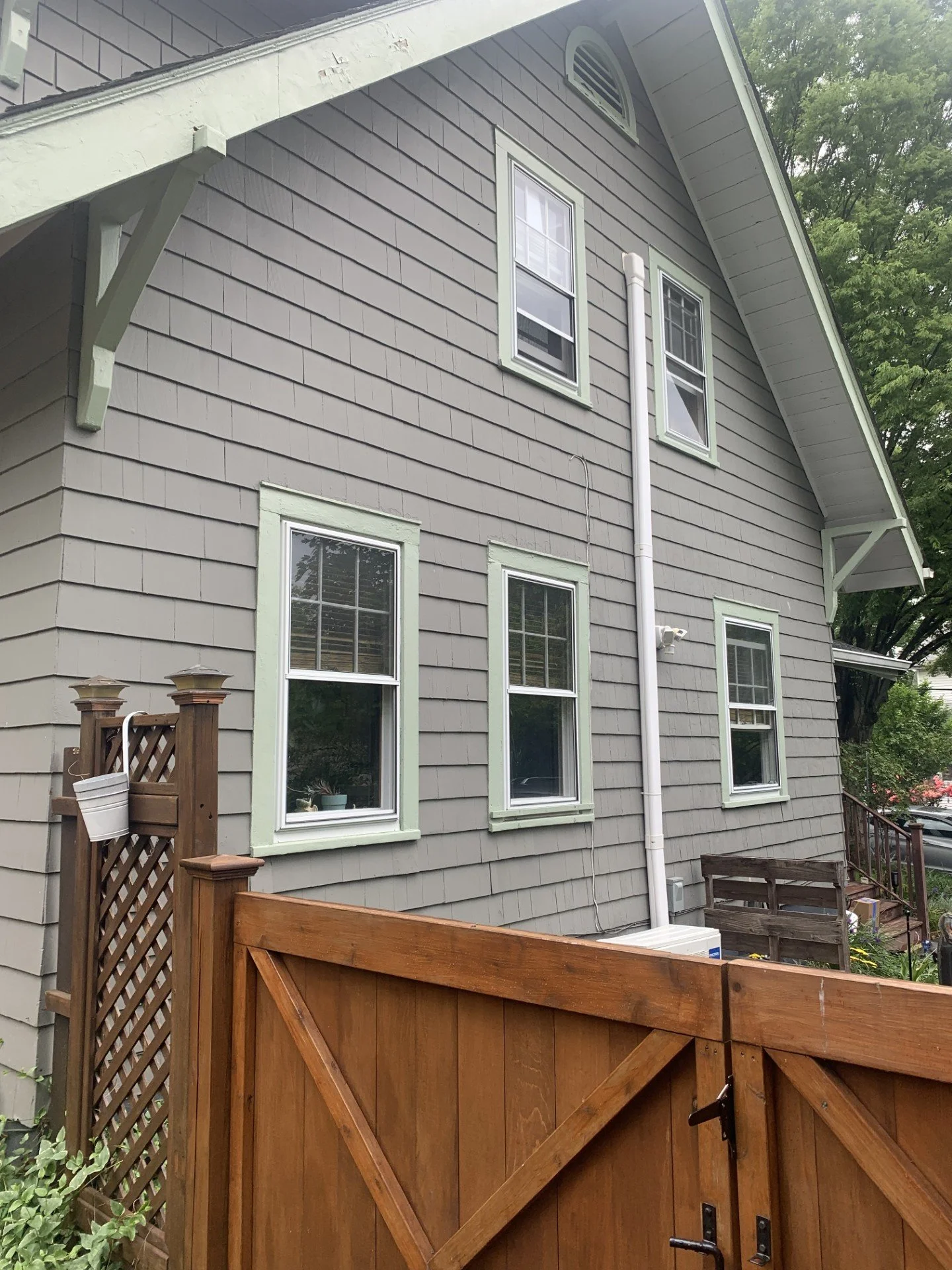 The side of a gray house with five windows, white trim, and a wooden fence in the foreground.