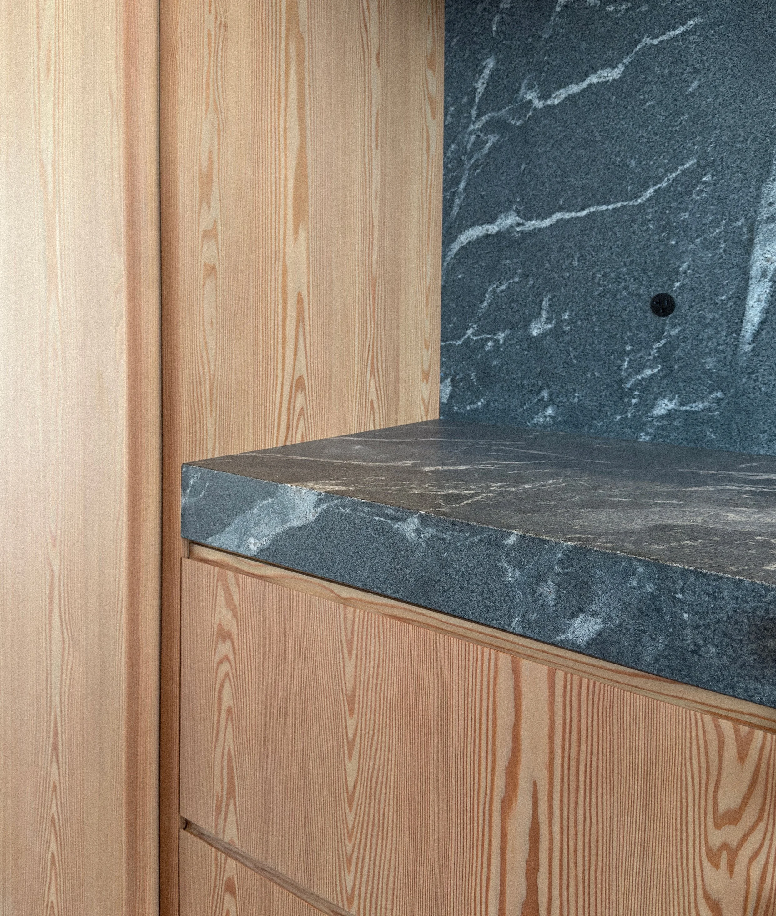 Close-up view of a kitchen or bathroom counter with a dark gray marble surface, matching marble backsplash, against natural wood-paneled wall.