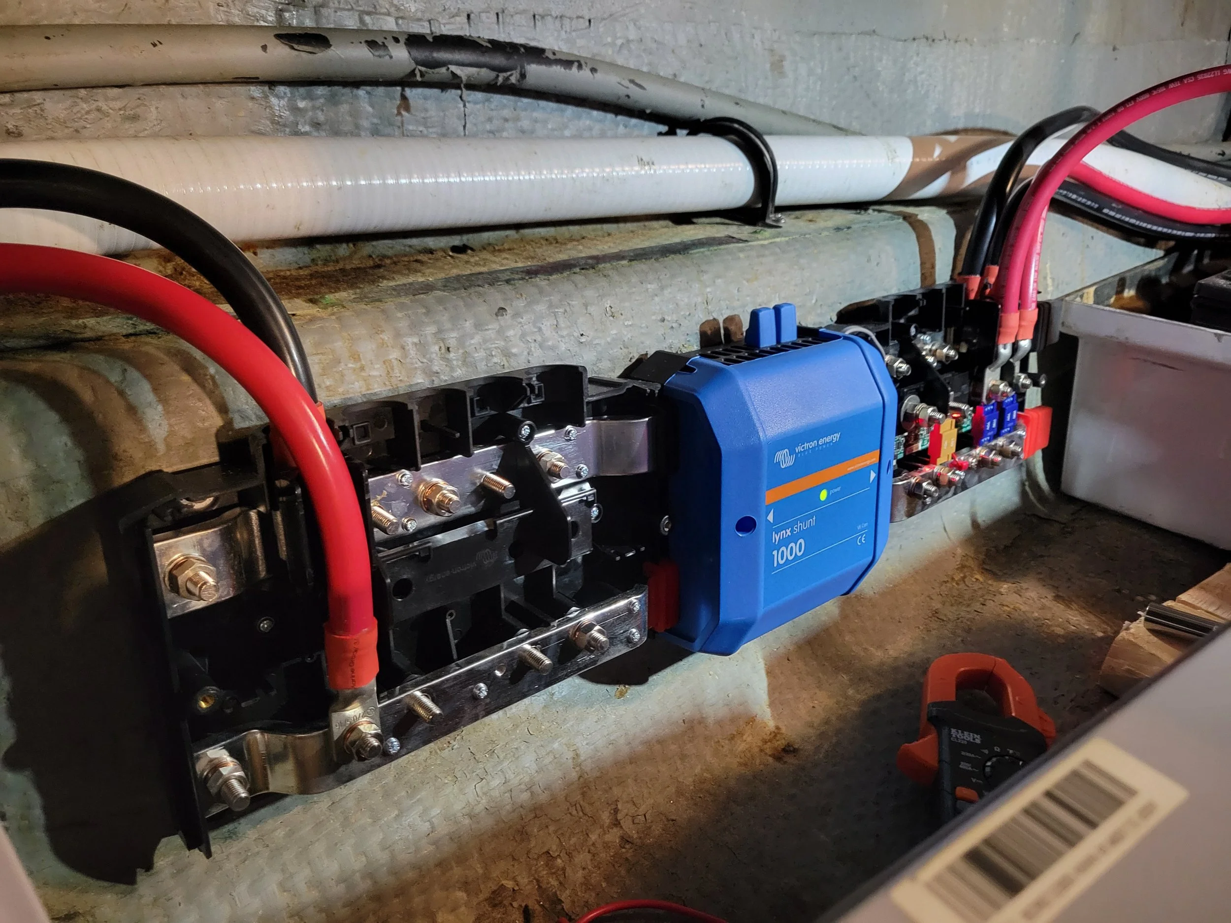 Electrical wiring and components, including a blue Victron Energy Xenon Shunt 1000, mounted on a concrete wall, with various wires and connections.