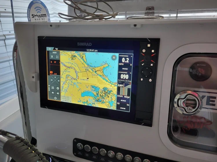 Navigational marine GPS screen showing a map with water and land, indicating geographic coordinates, depth, and weather information on a boat.