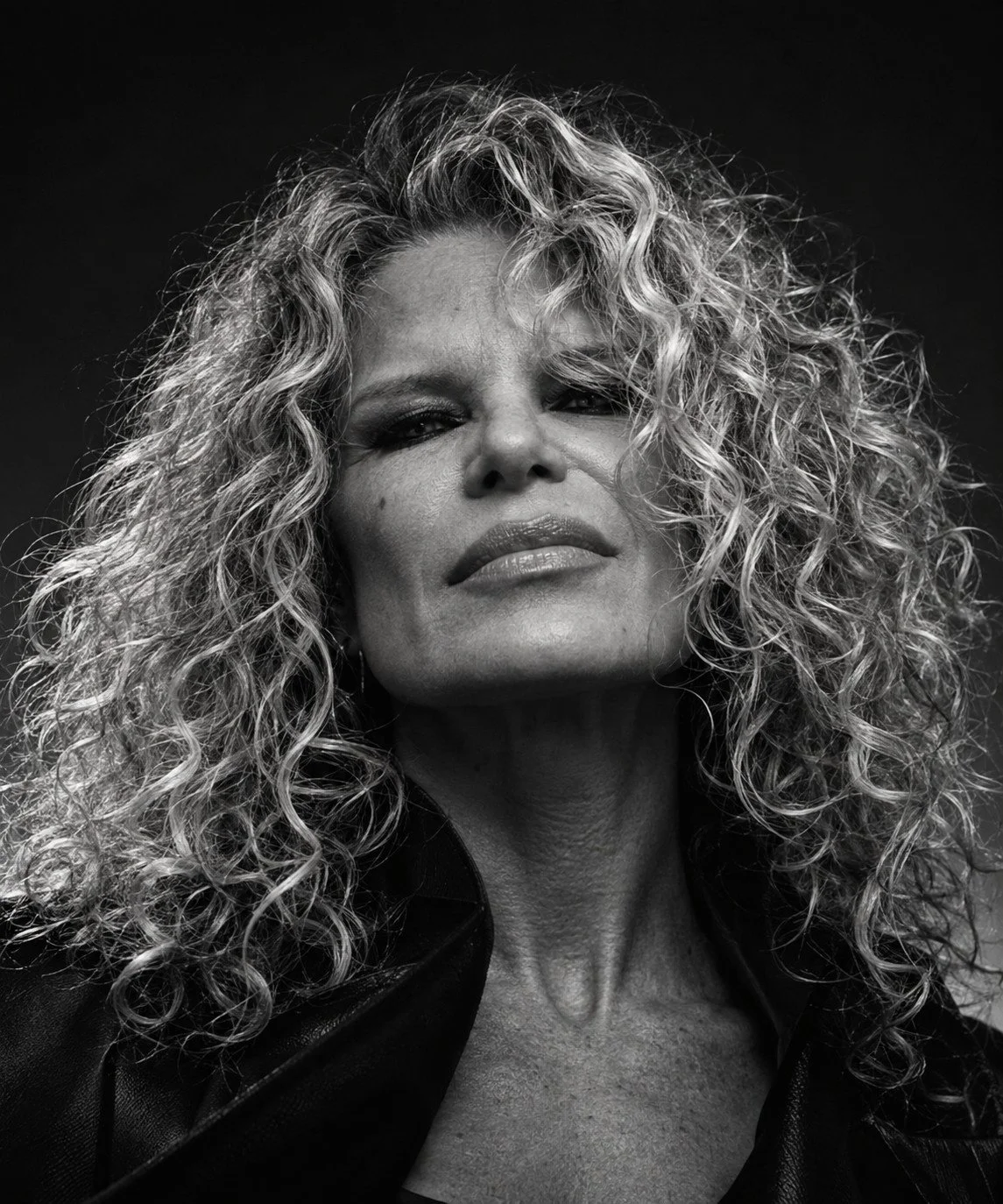 Chrisanna in a black leather jacket, curls lit against a dark background