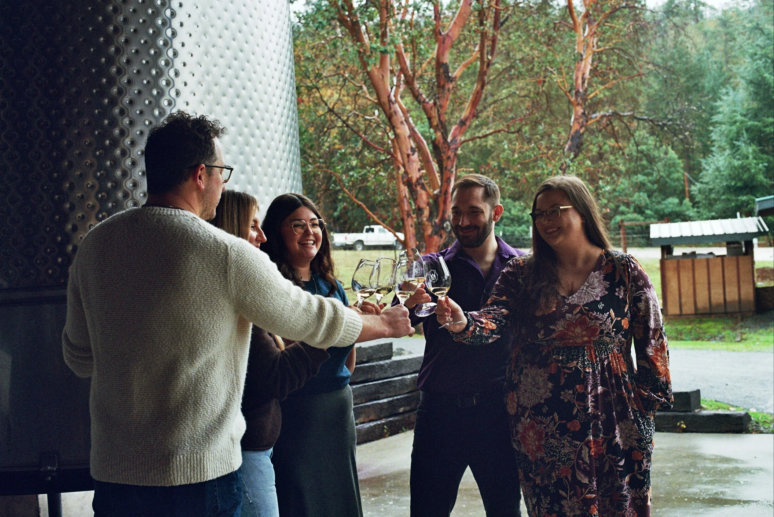 Wine tour guests cheers glasses in front of a fermentation tank on a wine tour, a great option for romantic winter getaways in Oregon.