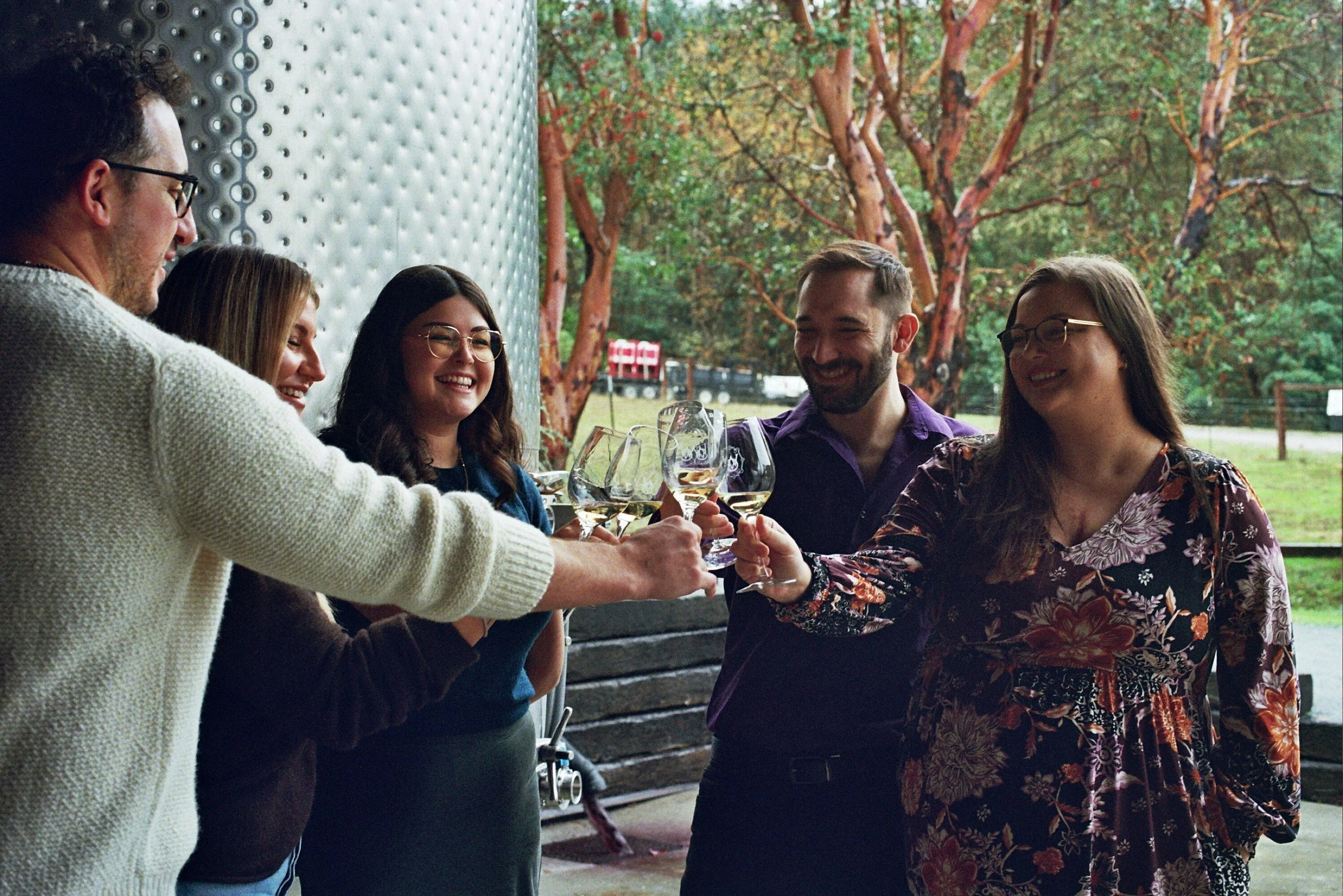 Wine tour guests cheers glasses in front of a fermentation tank on a wine tour, a great option for romantic winter getaways in Oregon.