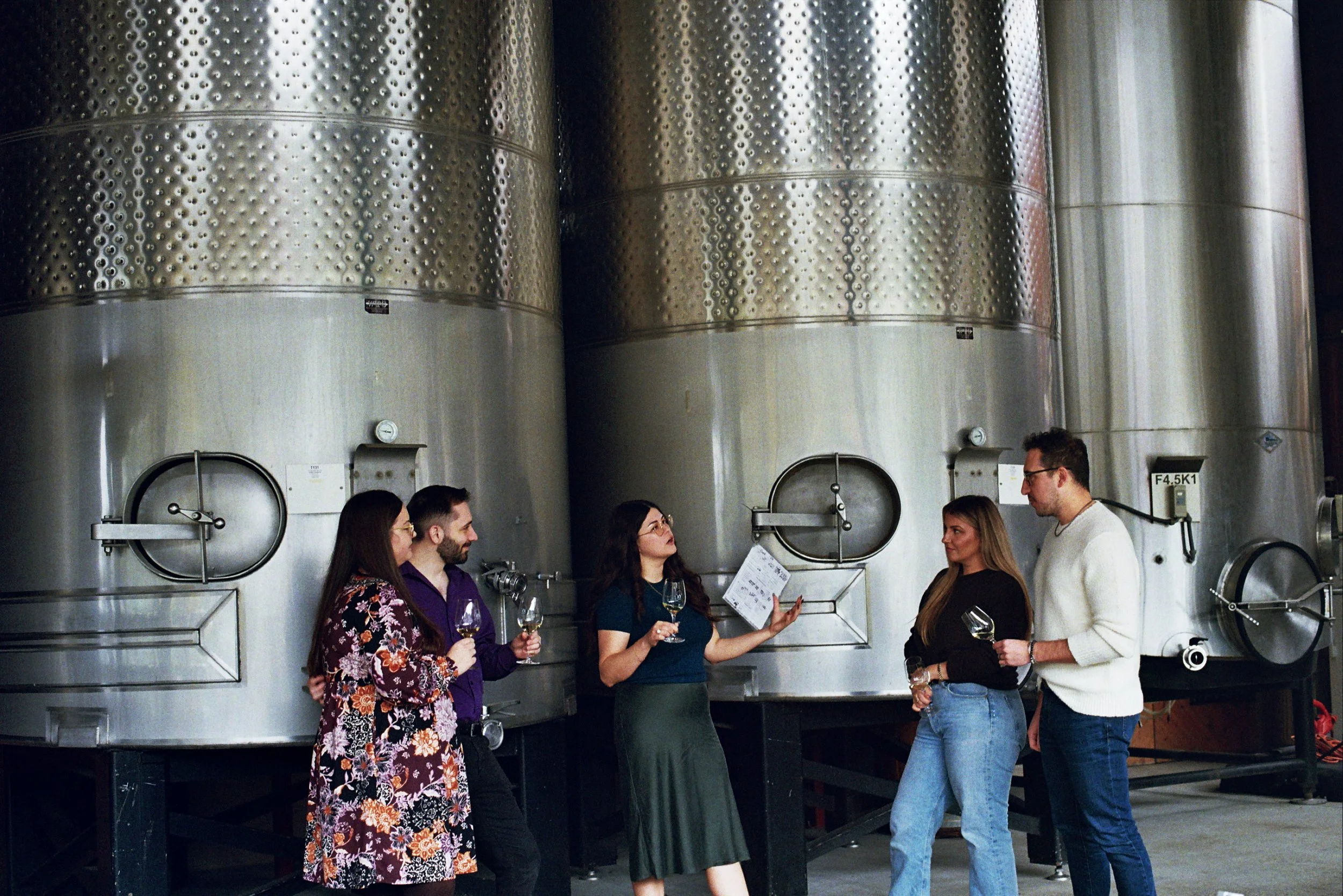 A group enjoying a wine tasting Southern Oregon listen their guide talk about the wine in front of tanks at a southern oregon winery.