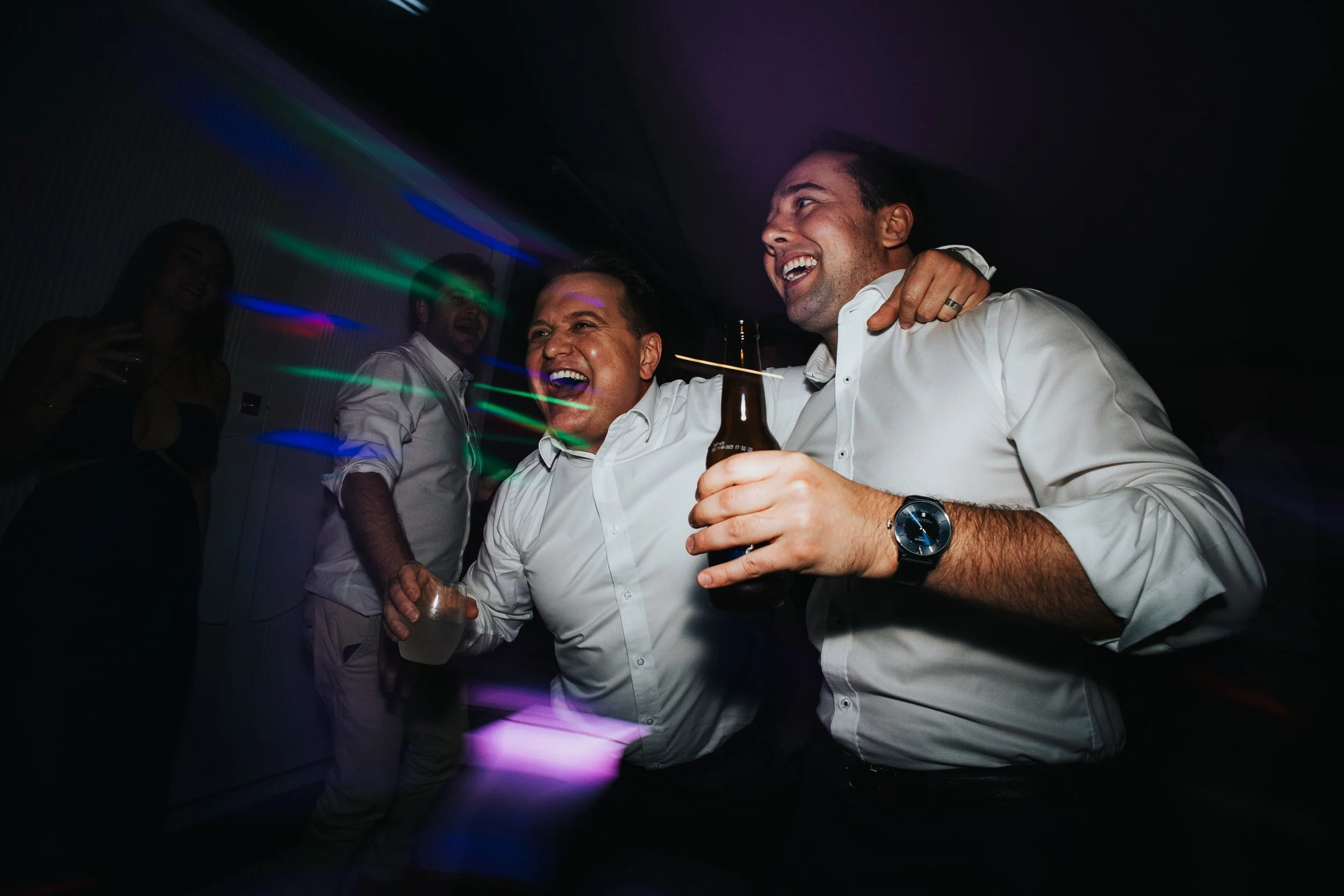 A group of friends enjoying at a party with colorful lights, laughing, and holding drinks.