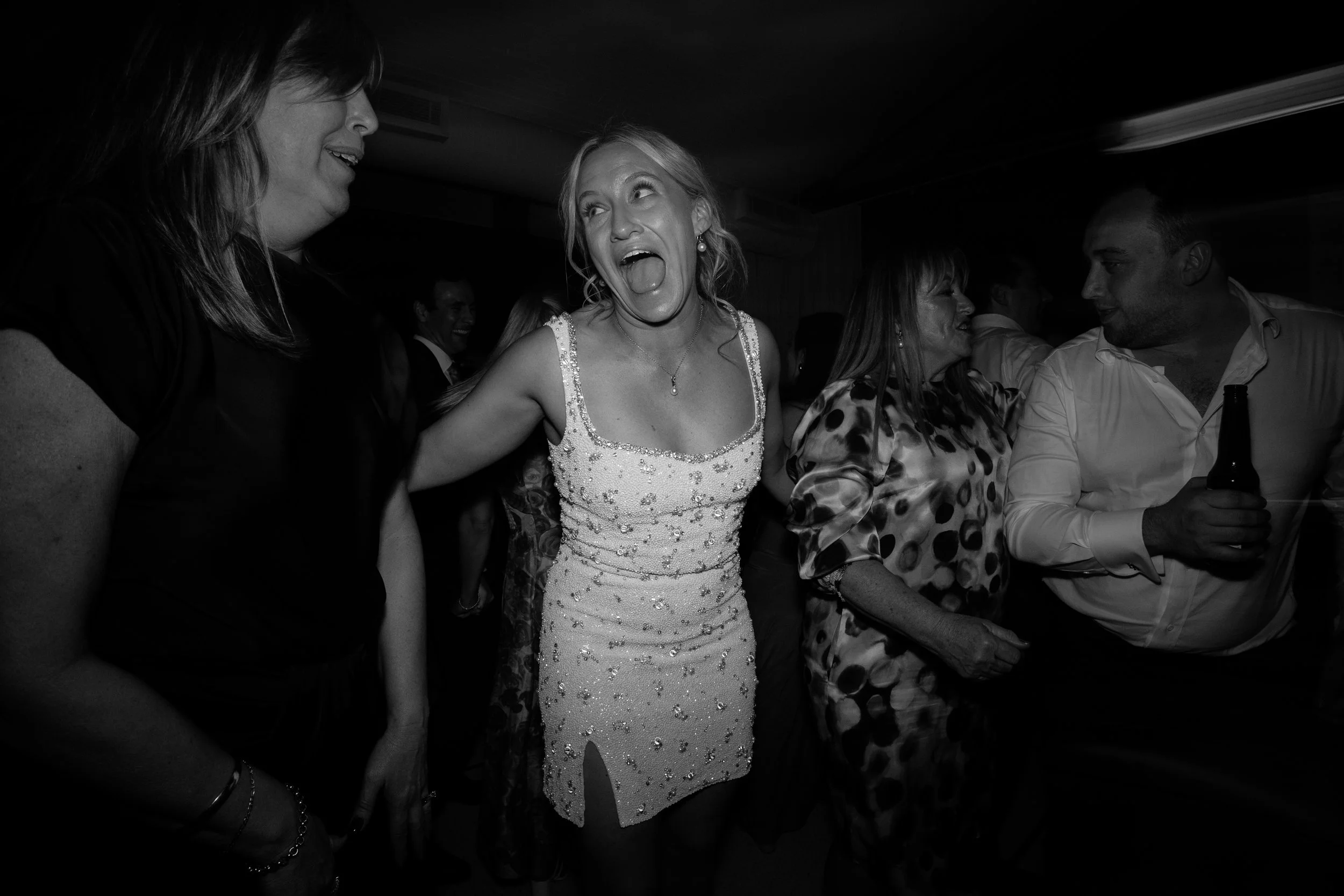 Group of people at a party, with a woman in a dress seemingly singing or talking enthusiastically.