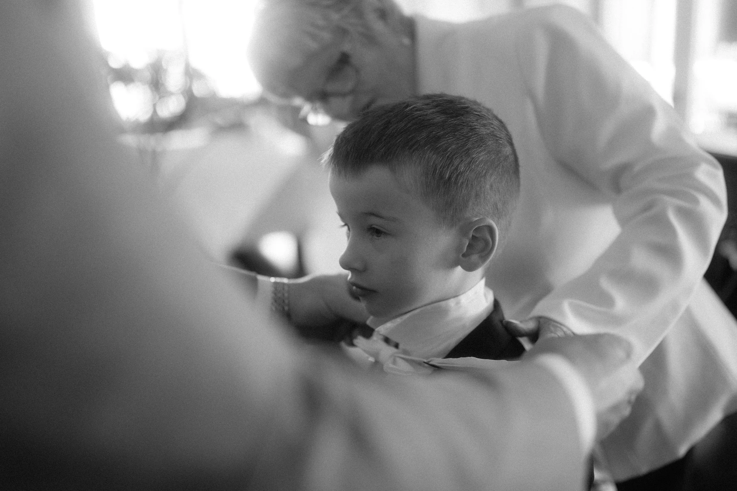 A black-and-white photo of a young boy with a close-cropped haircut, sitting with his head slightly tilted, as an adult woman in white attire, possibly a medical professional, examines or interacts with him, with a softly blurred background.