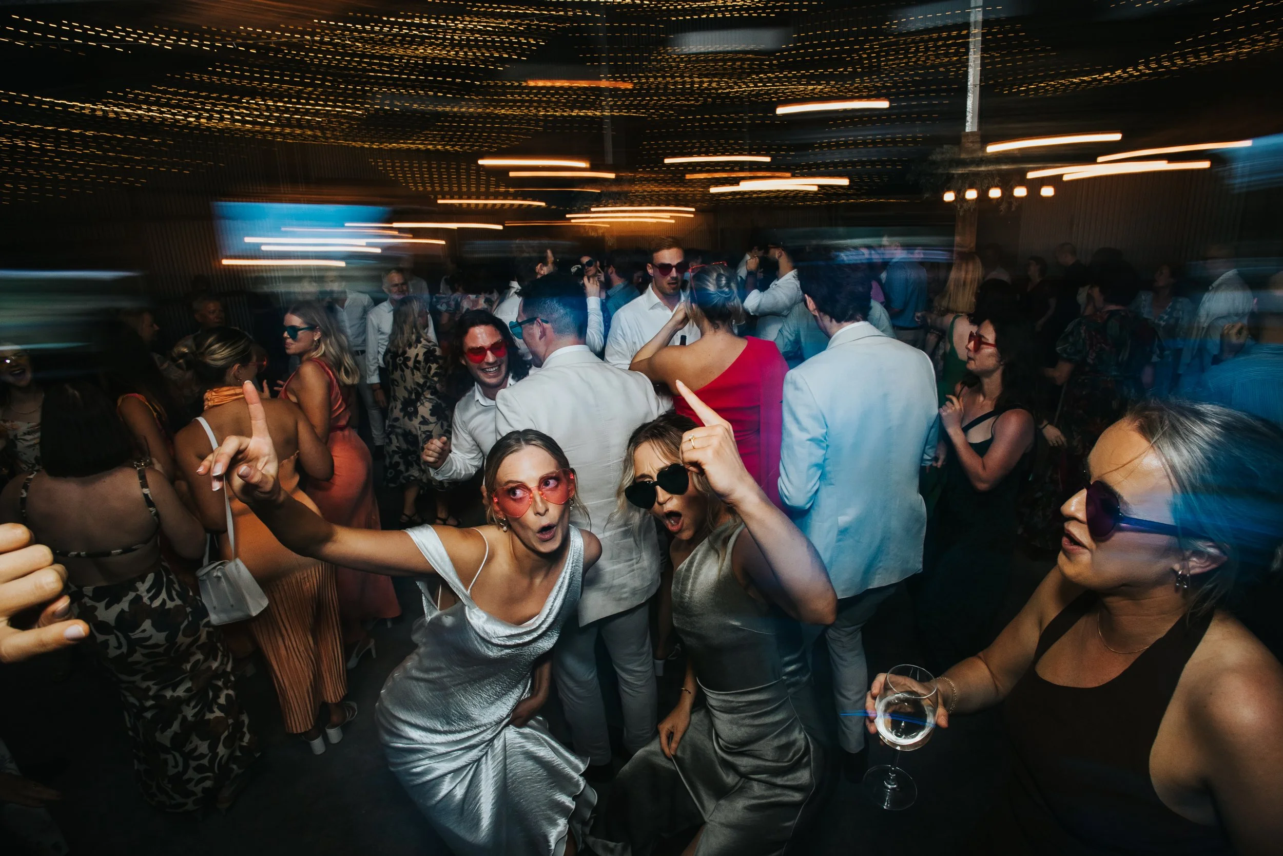 A crowded party with many people dancing and socializing under colorful lights.
