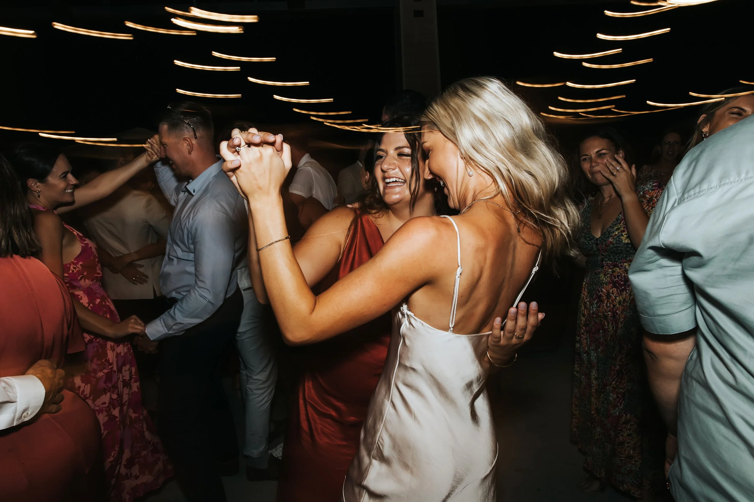 People dancing and enjoying themselves at a lively party or celebration in a dark room with streaks of light above.