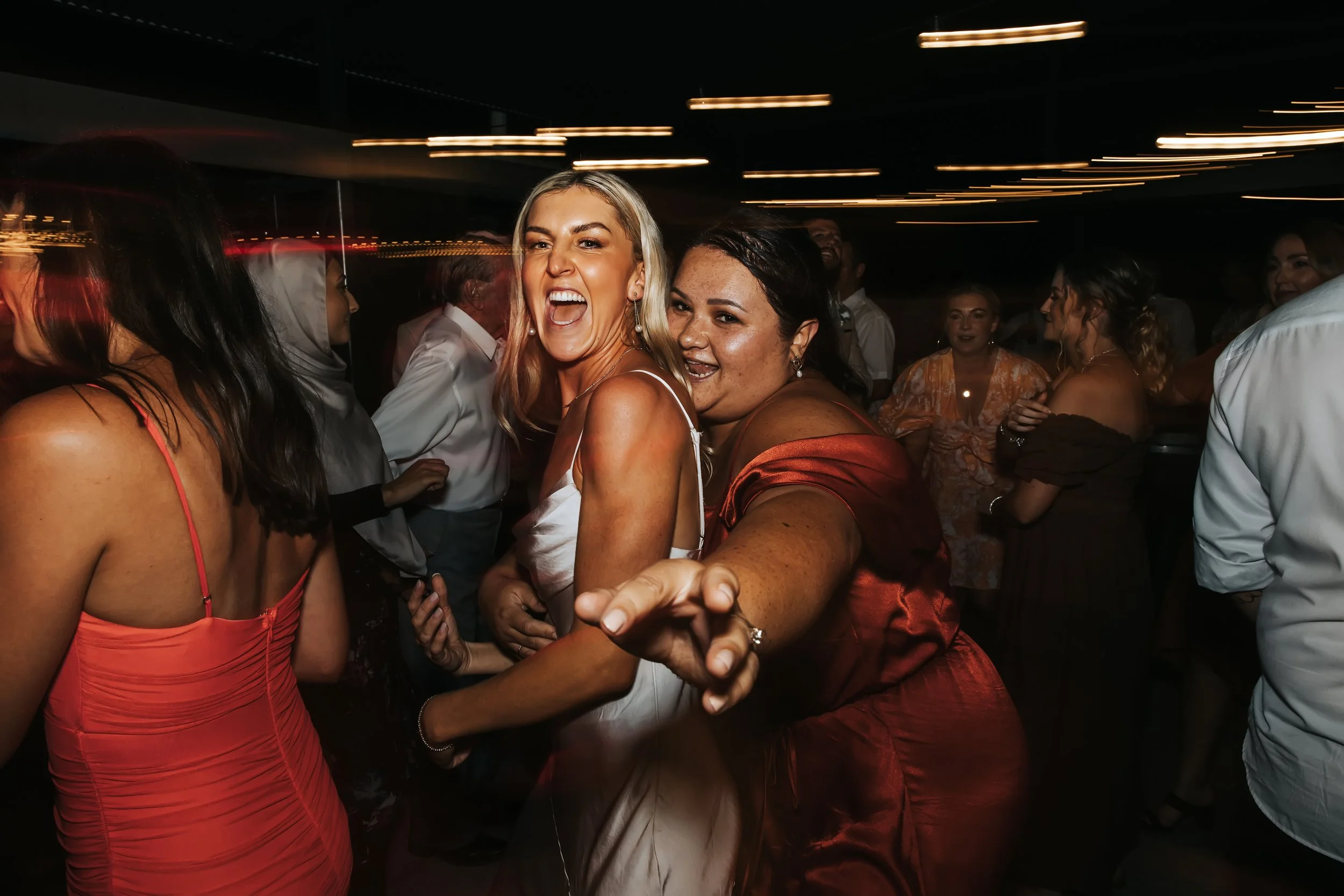 People dancing and having fun at a party in a dimly lit room with streaks of light from the ceiling lights.