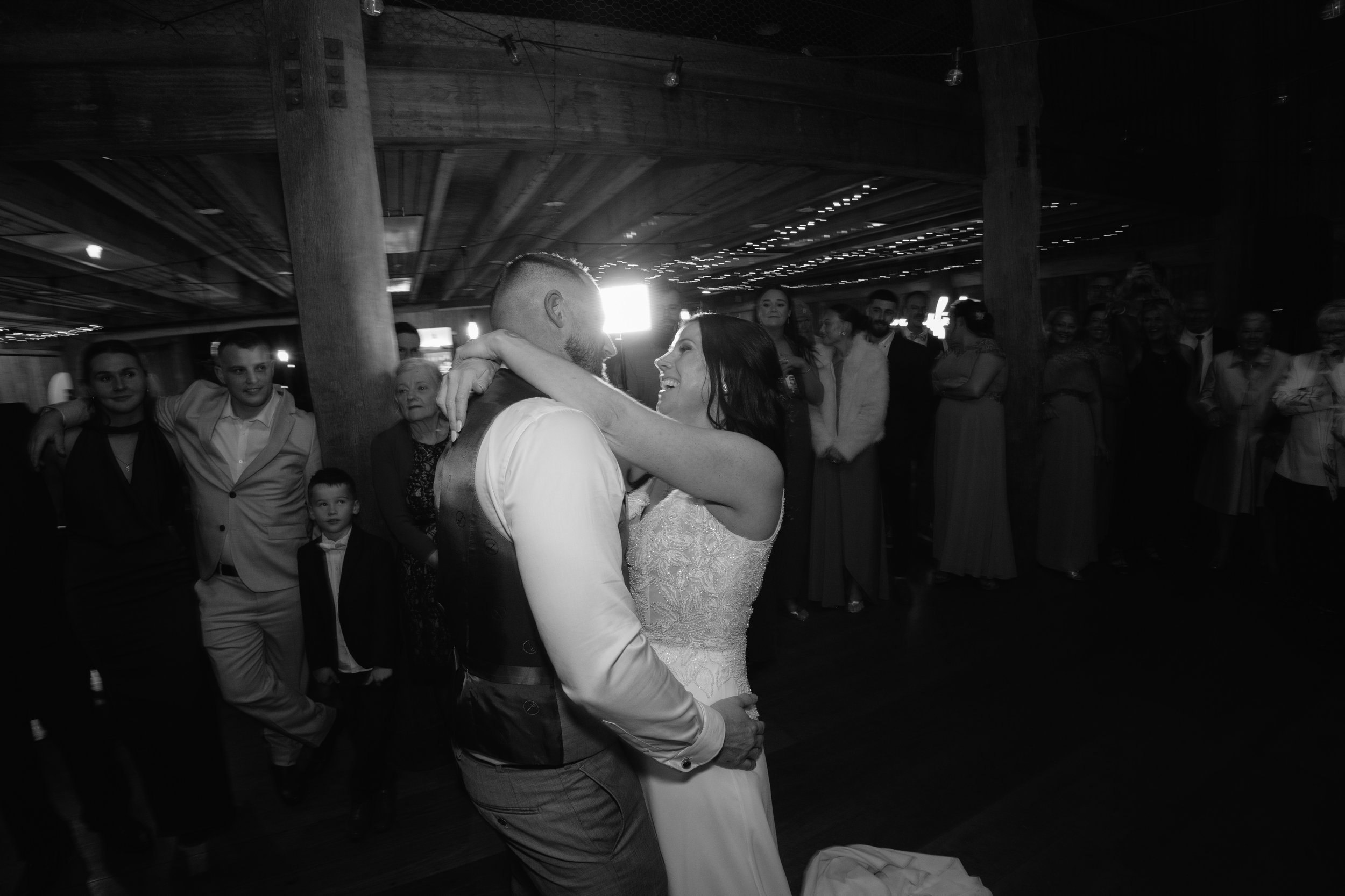 A newlywed couple dancing closely at their wedding reception, surrounded by guests in a decorated venue.