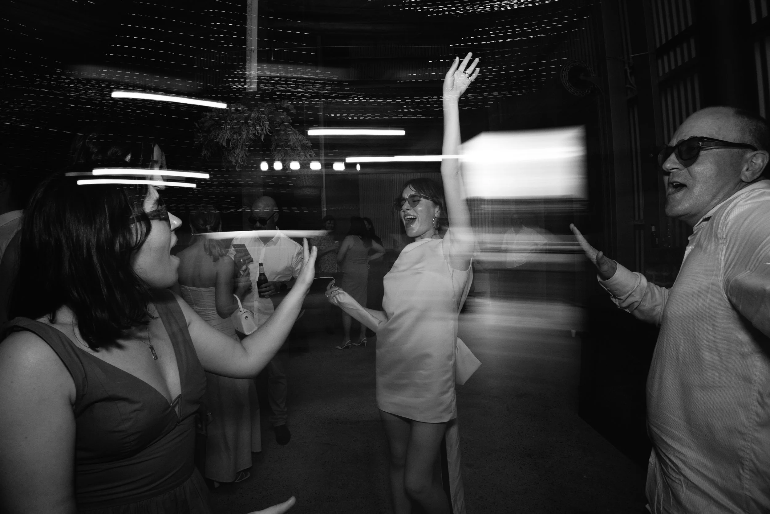 People dancing and socializing at a lively indoor event, captured with motion blur in black and white.