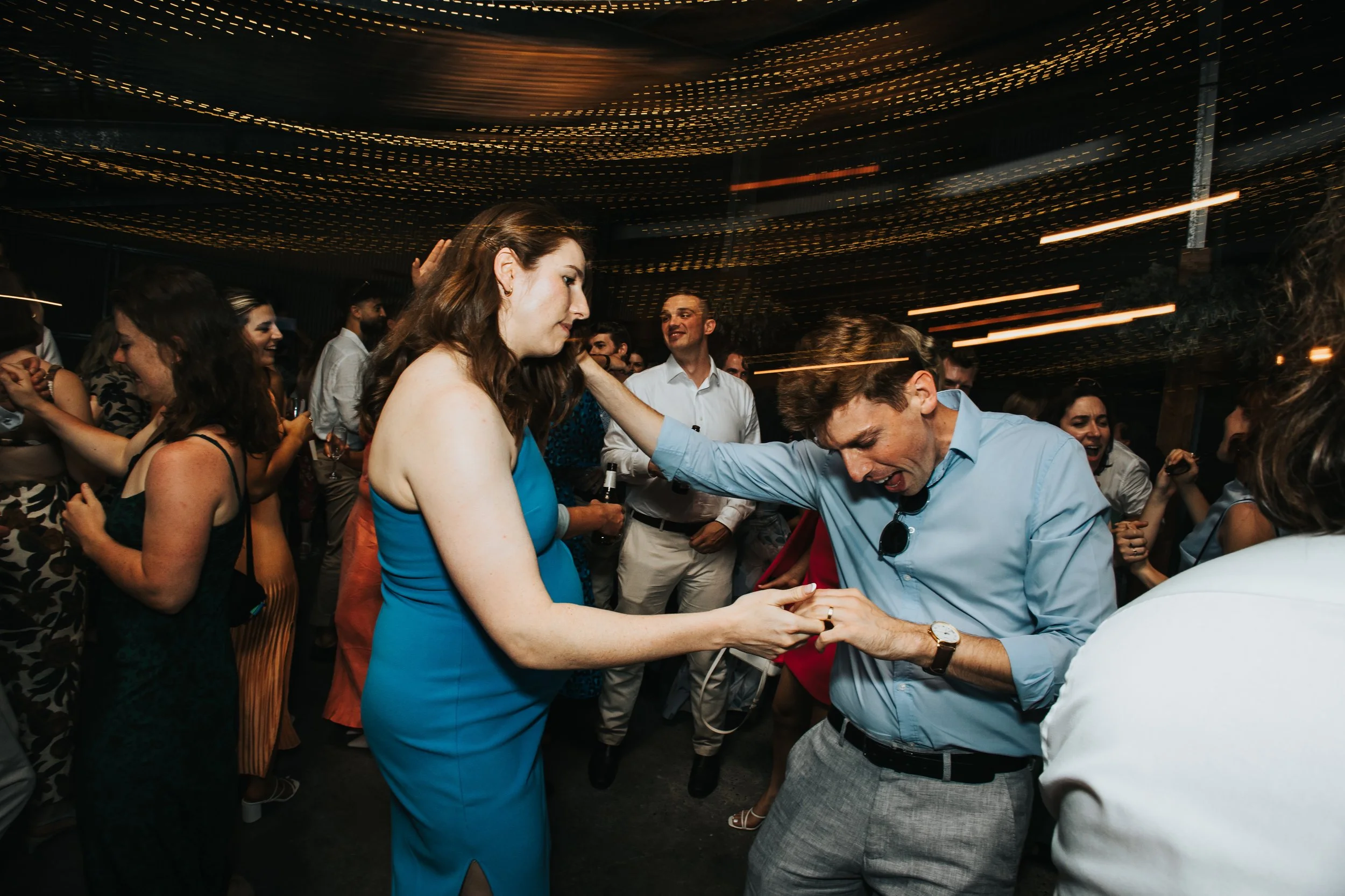 People dancing and socializing at a lively party with string lights overhead.