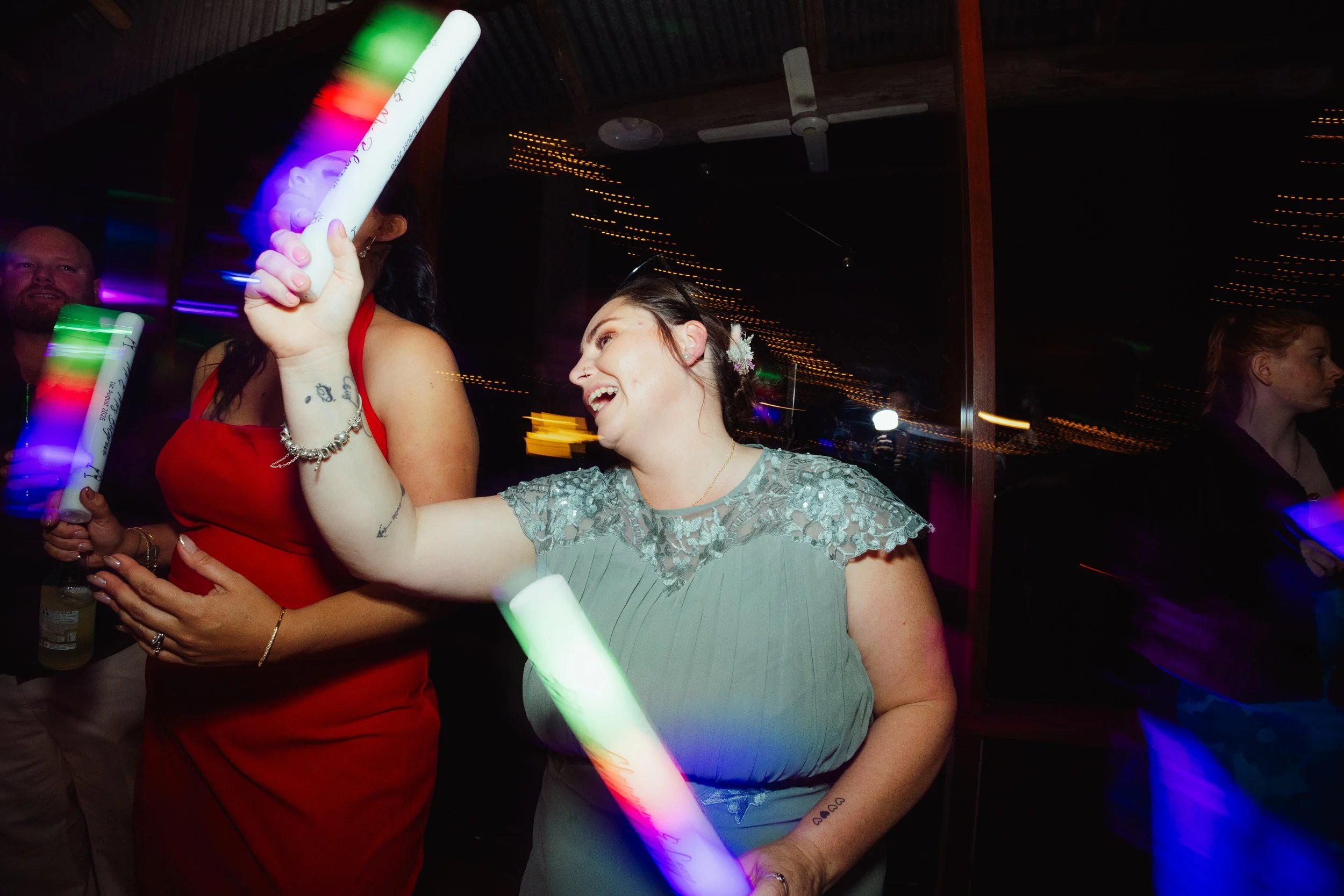 People dancing and enjoying themselves at a party, holding glow sticks, with a dark background and colorful lights.
