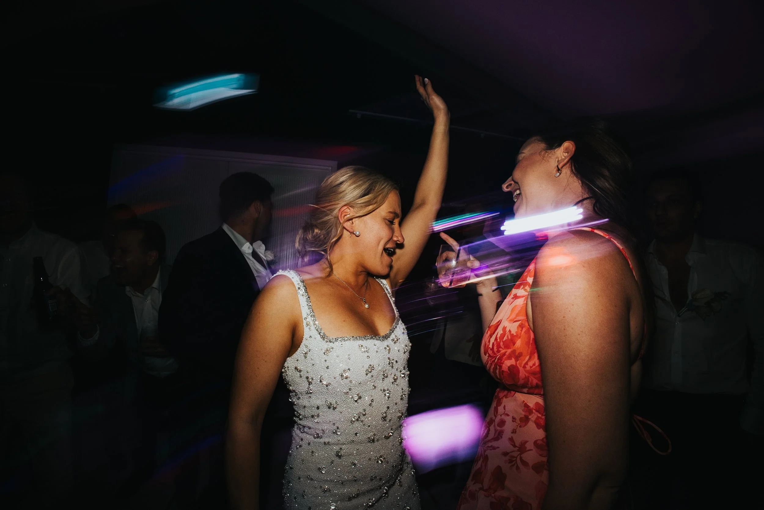 Two women dancing and enjoying themselves at a party or celebration, with other people in the background.