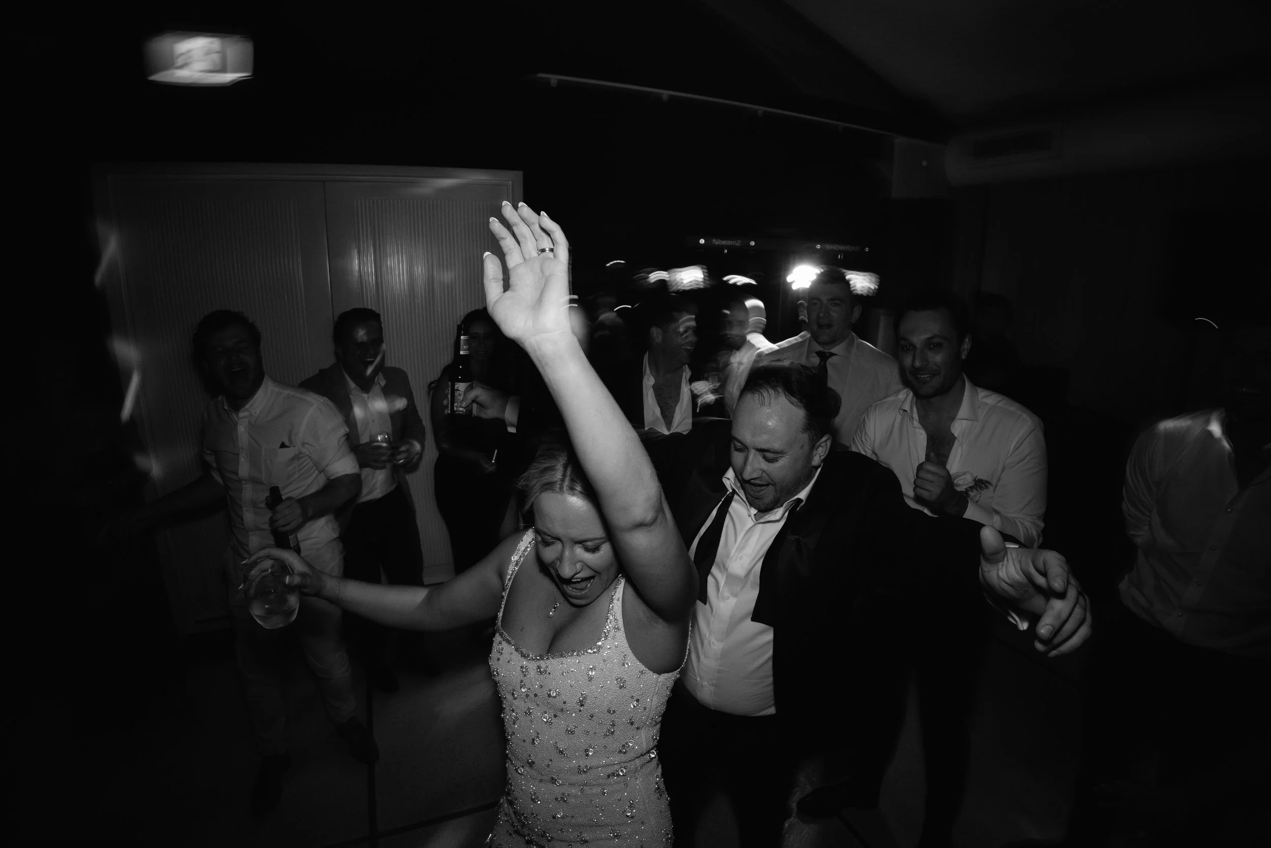 Group of people dancing and celebrating at a party, with a woman in the foreground holding a drink and smiling.