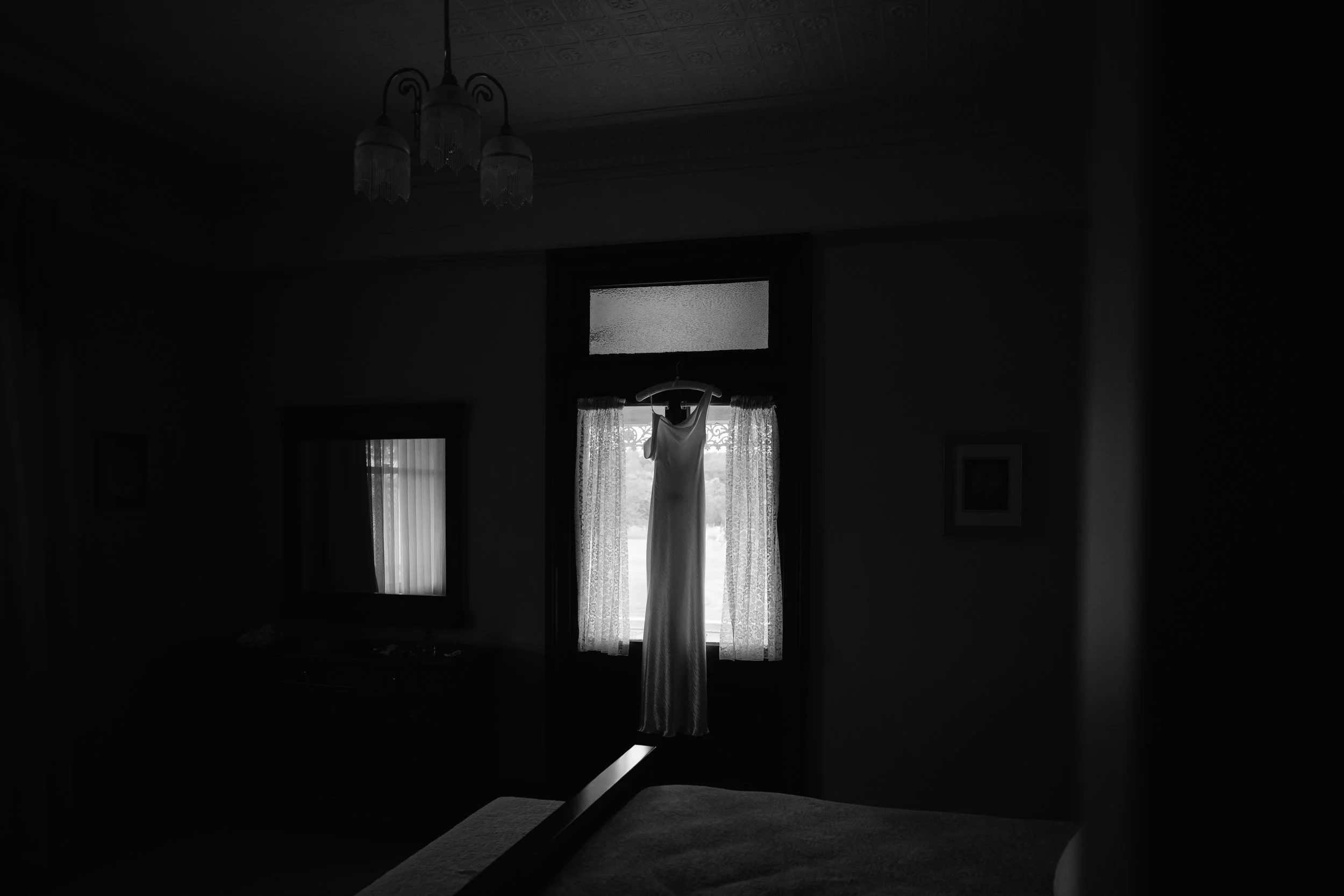 A wedding dress hanging in front of a window in a dimly lit room.