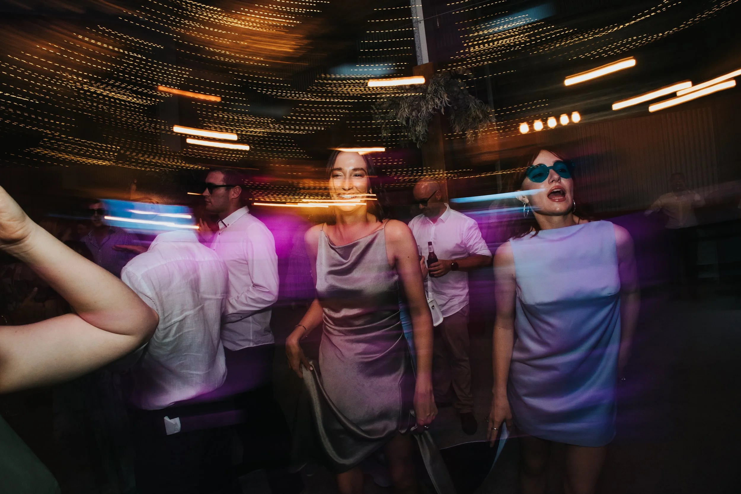 People dancing and having fun in a lively, colorful party or nightclub with streaks of motion light and reflections creating a vibrant atmosphere.