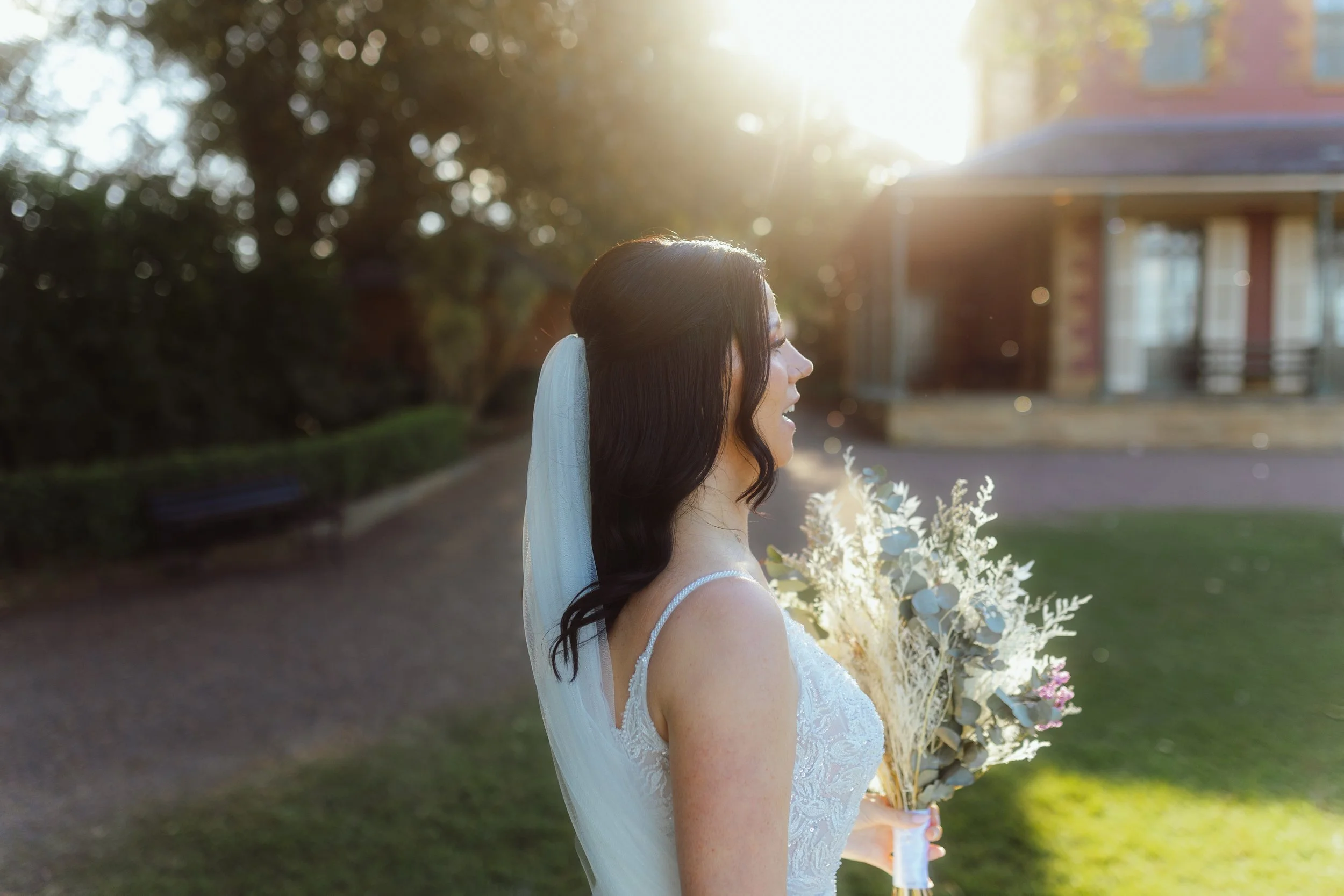 A woman in a wedding dress holding a bouquet of flowers outdoors at sunset.