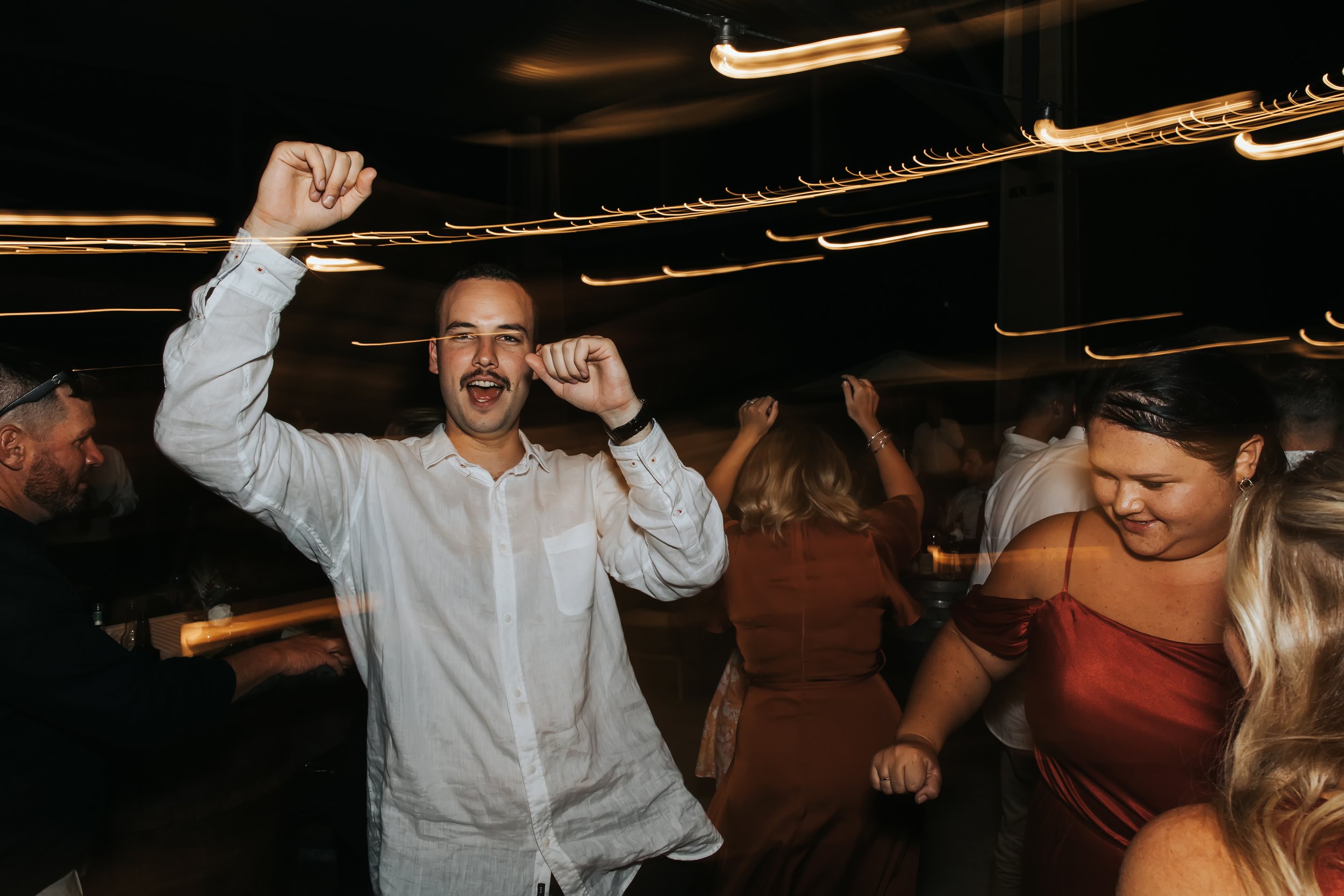 A man in a white shirt dancing or celebrating at a party or celebration event with other people in the background.