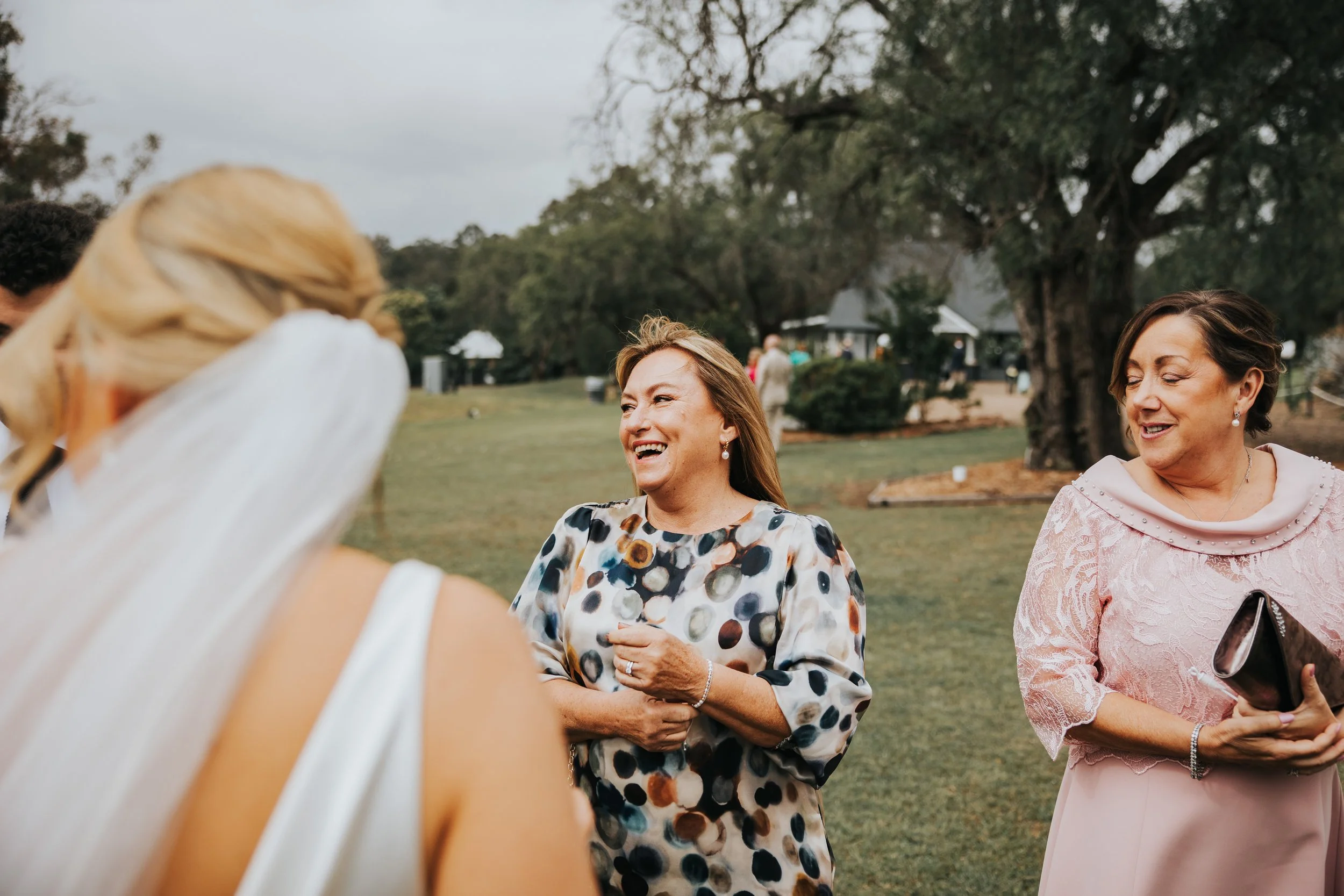 A group of women talking outdoors at a gathering or event, with one woman smiling and wearing a dress with a polka dot pattern and celebrating.